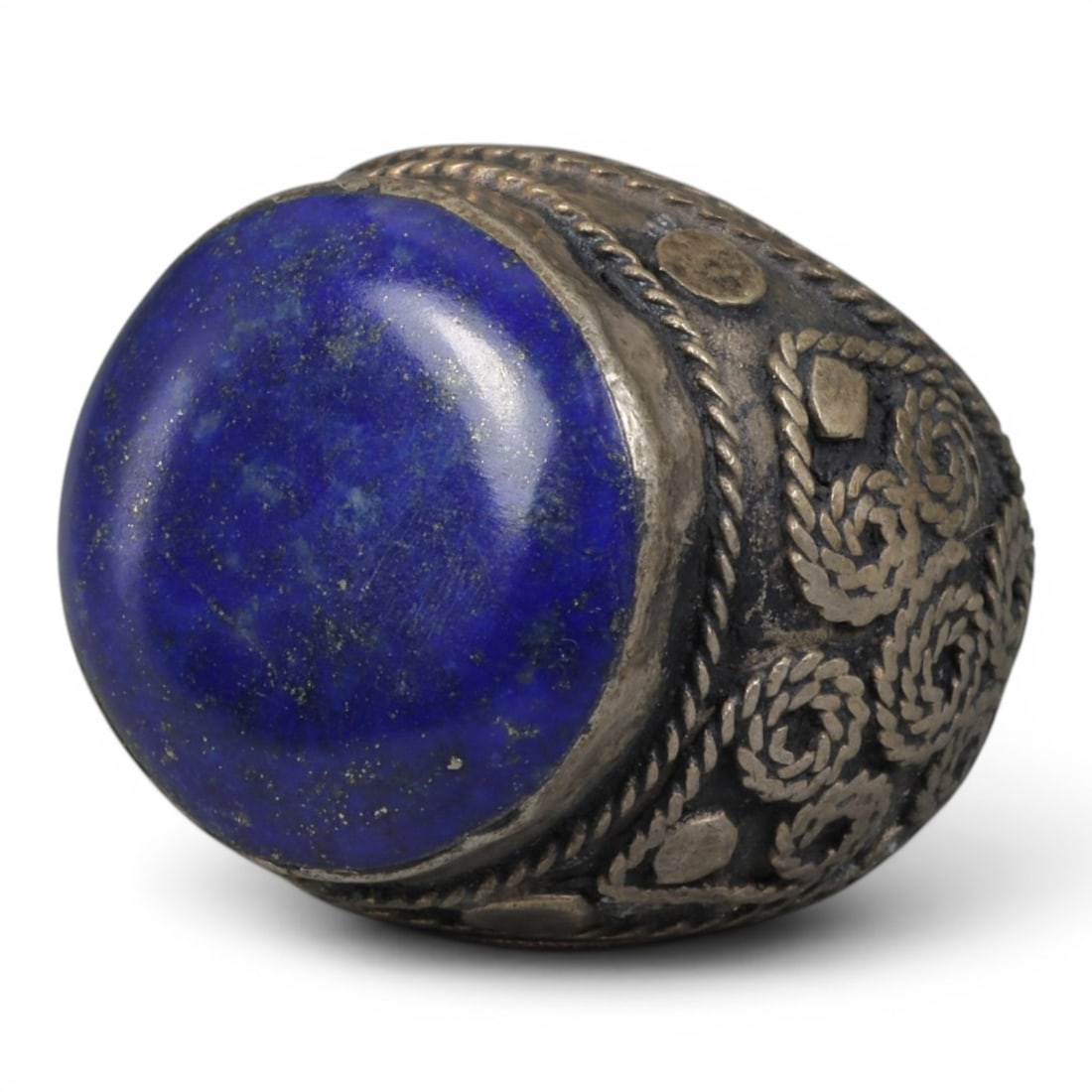 Antique Central Asian Silver and Lapis Lazuli Tribal Ring, 19th-Early 20th Century, 55AJ: The ring is set with a large, smooth cabochon lapis lazuli stone, exhibiting natural pyrite inclusions within its deep blue matrix. The silver mount is decorated with pseudo-filigree wirework and appl