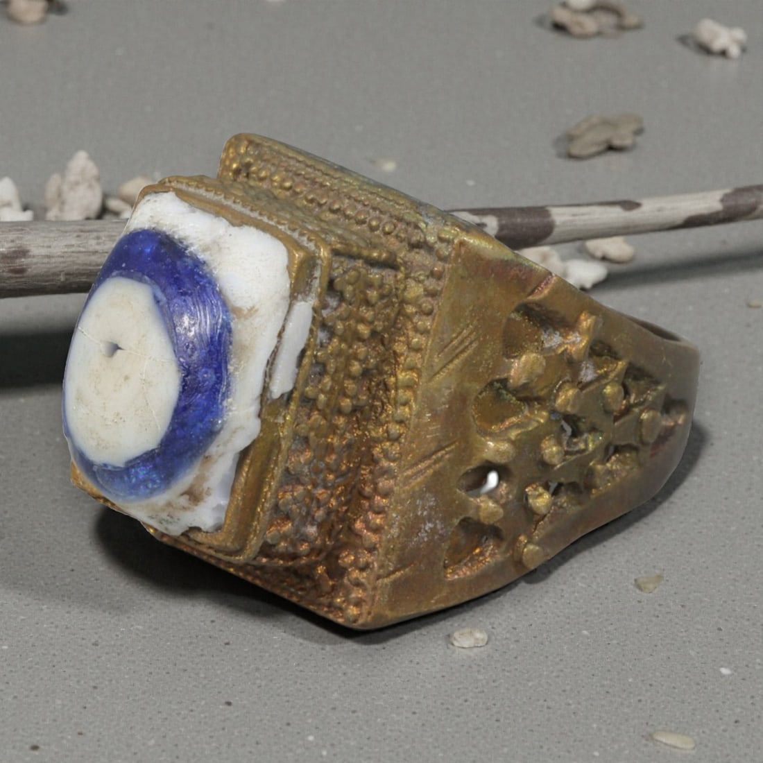 Antique Qajar Dynasty Gilt Evil Eye Ring, US Size 10, 14AJ: A gilt-metal ring of the Qajar period, US ring size 10, featuring a rectangular bezel set with a blue-and-white evil-eye glass inlay. The ring is richly detailed with multiple layers of ornamentation: