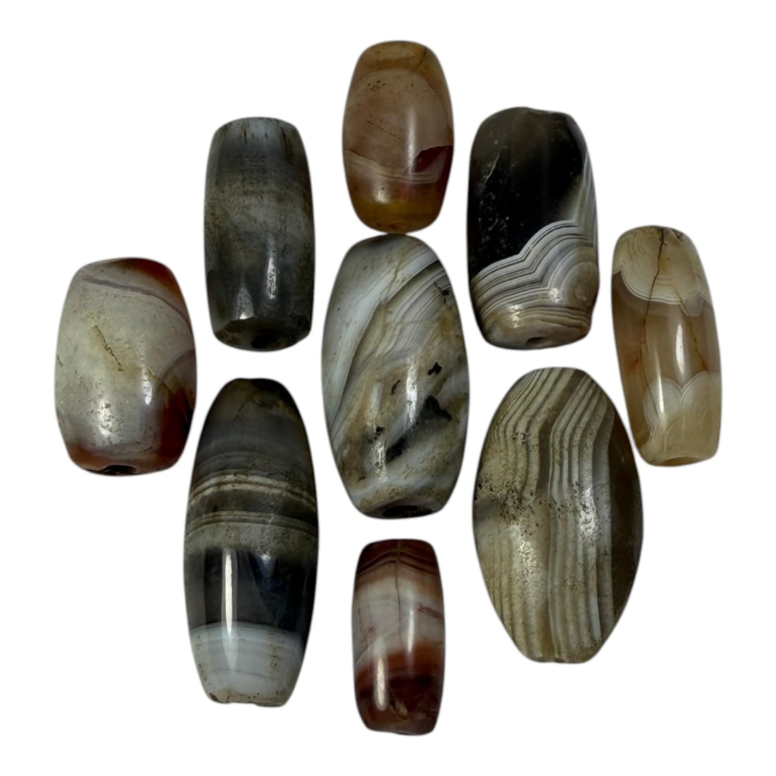 A Lot of 9 Himalayan Banded Agate Beads, Ancient to Antique Period, 49AN: Comprising lot of barrel and ovoid beads, each carved from banded agate with natural tonal variations, many displaying characteristic concentric, linear, and dendritic patterns. The surfaces exhibit s