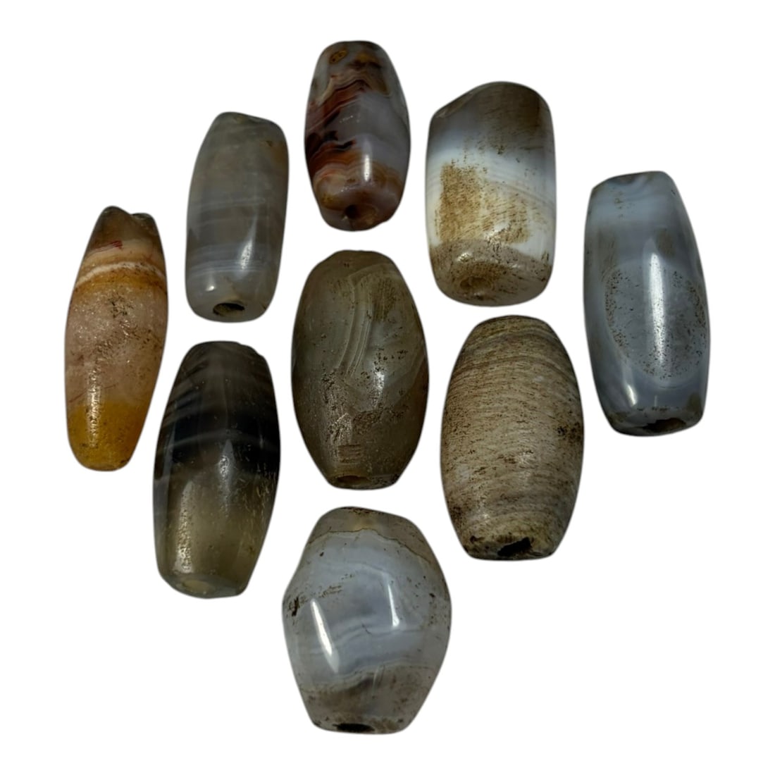 A Lot of 9 Himalayan Banded Agate Beads, Ancient to Antique Period, 52AN: Comprising lot of barrel and ovoid beads, each carved from banded agate with natural tonal variations, many displaying characteristic concentric, linear, and dendritic patterns. The surfaces exhibit s