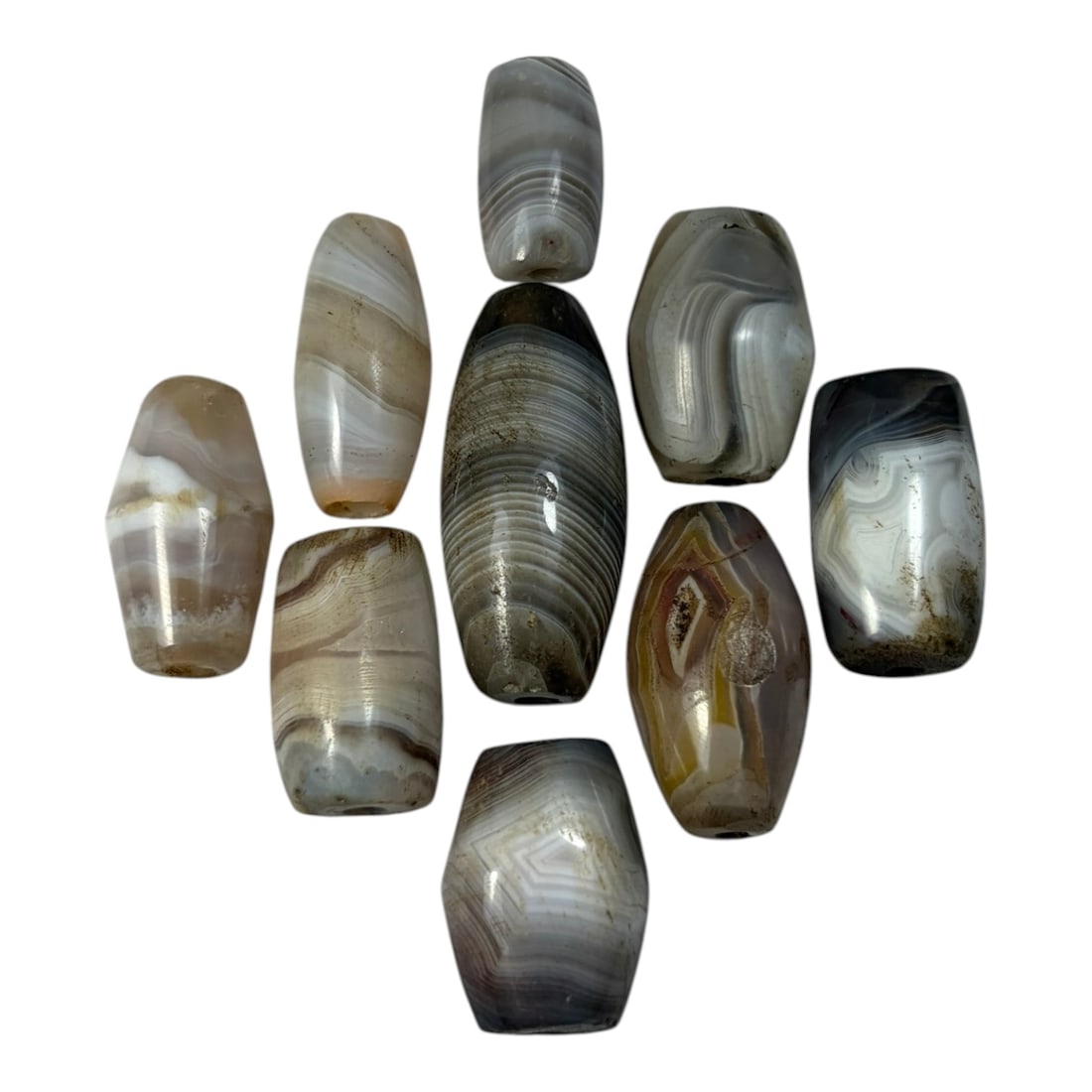 A Lot of 9 Himalayan Banded Agate Beads, Ancient to Antique Period, 41AN: Comprising lot of barrel and ovoid beads, each carved from banded agate with natural tonal variations, many displaying characteristic concentric, linear, and dendritic patterns. The surfaces exhibit s