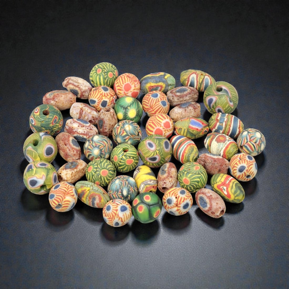 A Lot of 44 Vintage Artisan Glass Trade Beads, 30WM: A curated collection of 44 glass trade beads, primarily spherical and slightly oval in form, all with central perforations. The beads feature intricate patterns including eye motifs, striped designs, 