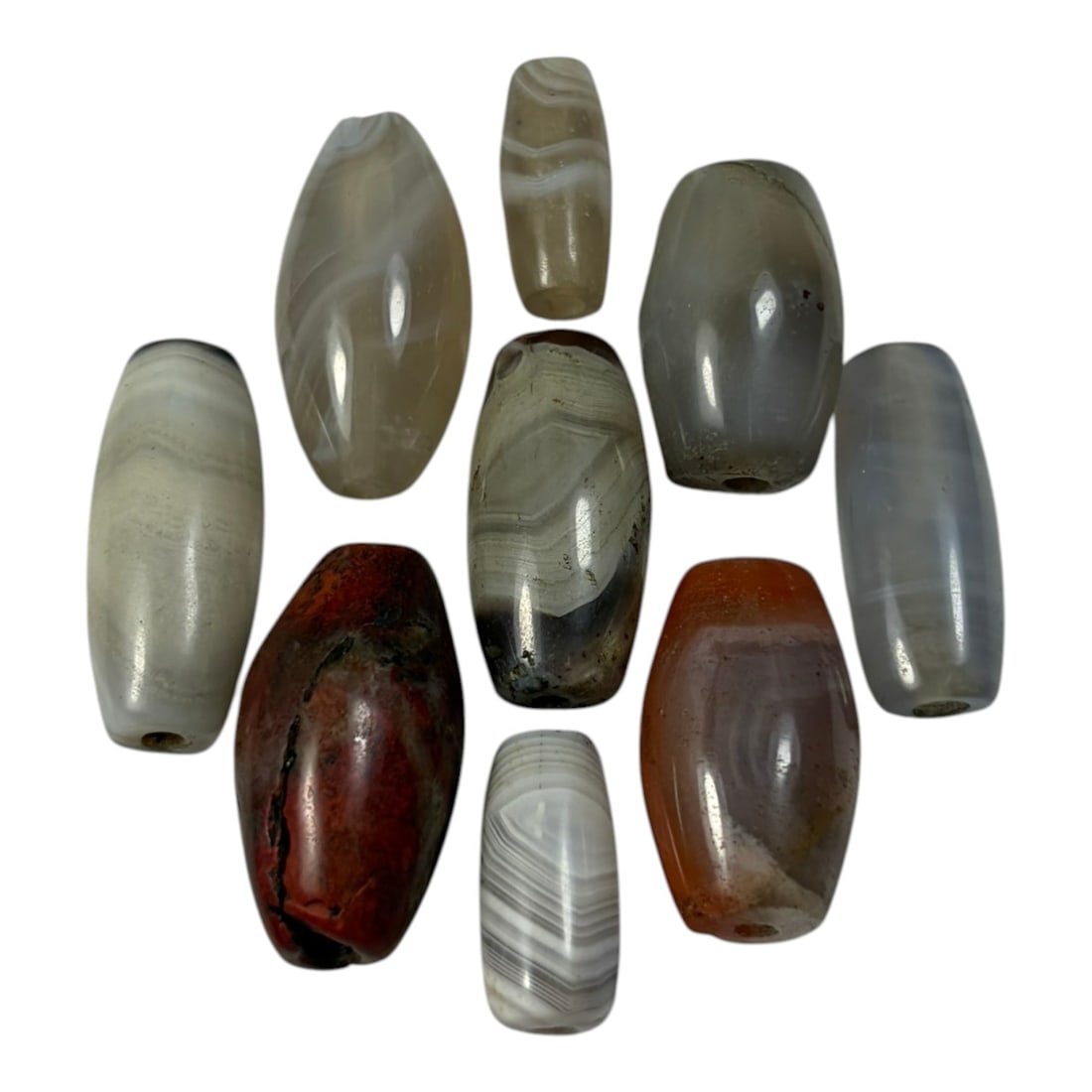 A Lot of 9 Himalayan Banded Agate Beads, Ancient to Antique Period, 42AN: Comprising lot of barrel and ovoid beads, each carved from banded agate with natural tonal variations, many displaying characteristic concentric, linear, and dendritic patterns. The surfaces exhibit s