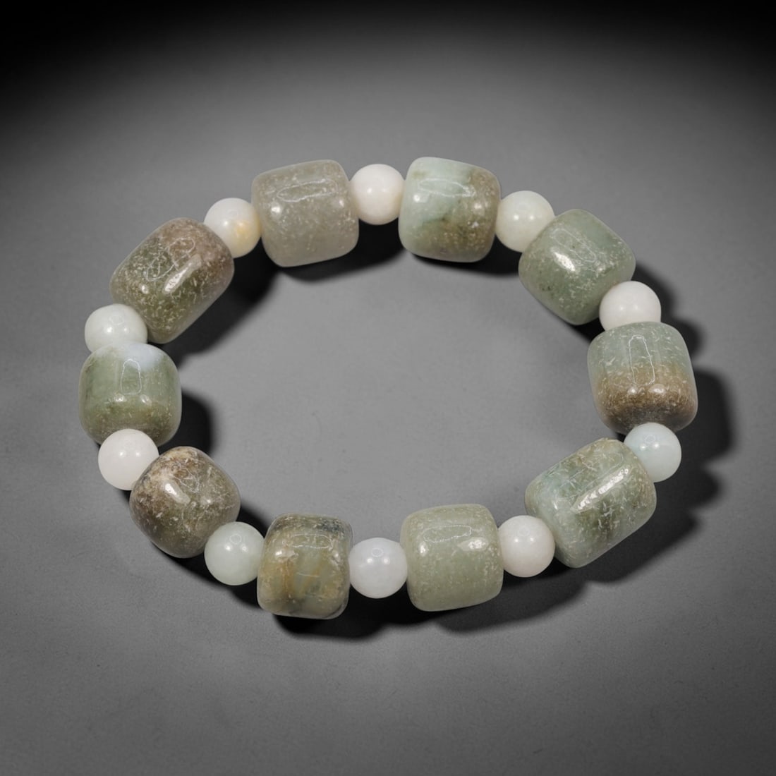 A Chinese Jadeite Jade Bead Bracelet, 20th Century, 42ZK: Composed of a single strand of cuboid and spherical jadeite jade beads forming a circular bracelet. The cuboid beads display natural tonal variation from pale green to deep green, with visible interna