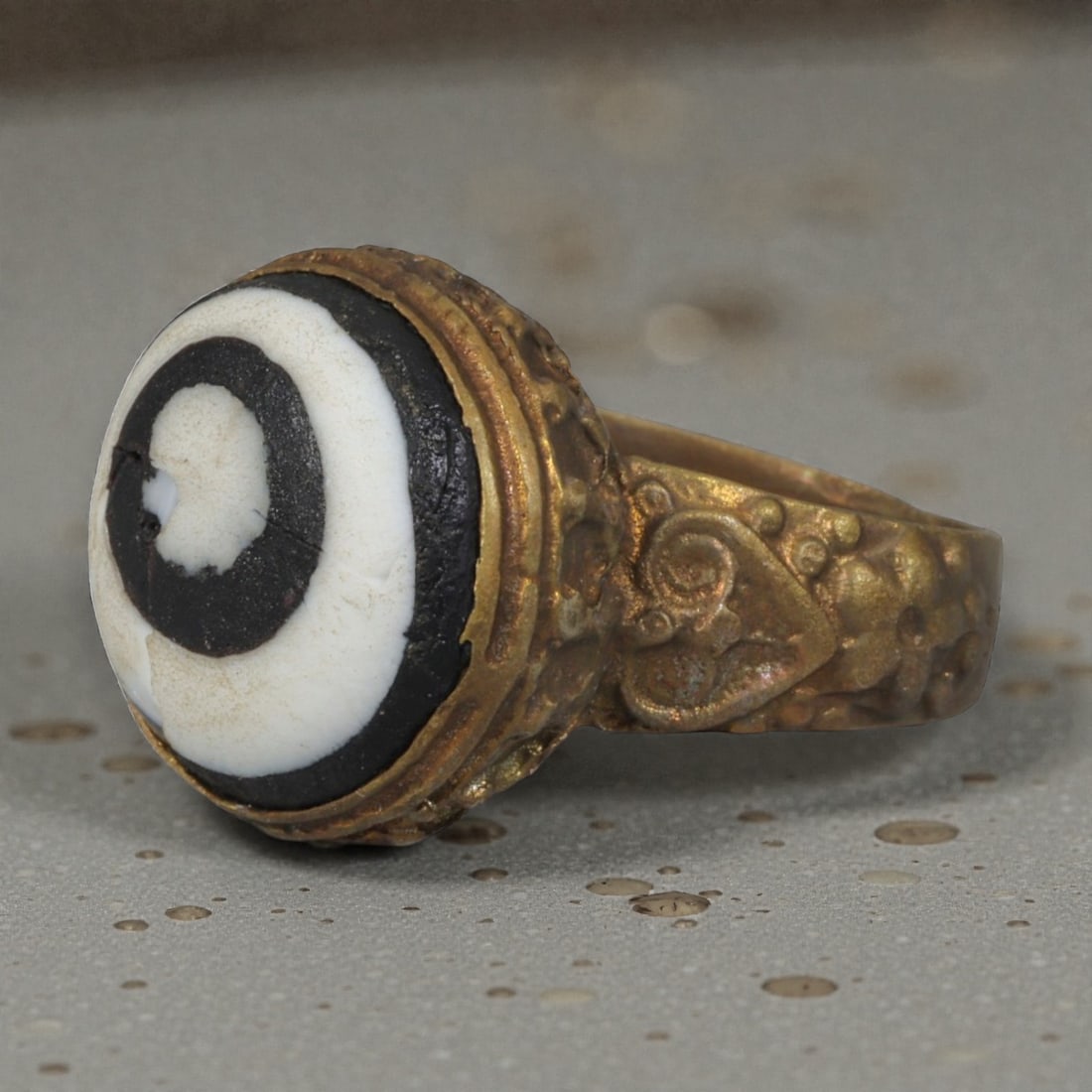 Antique Qajar Dynasty Gilt Evil Eye Ring, US Size 8.5, 10AJ: A gilt-metal ring of the Qajar period, US ring size 8.5, featuring a large domed evil-eye glass inlay with a bold concentric black-and-white design. The bezel is decorated with a textured, bubble-like