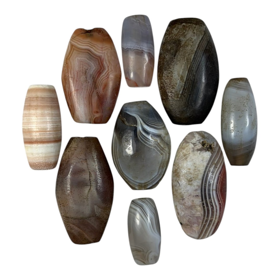 A Lot of 9 Himalayan Banded Agate Beads, Ancient to Antique Period, 26YD: Comprising lot of barrel and ovoid beads, each carved from banded agate with natural tonal variations, many displaying characteristic concentric, linear, and dendritic patterns. The surfaces exhibit s