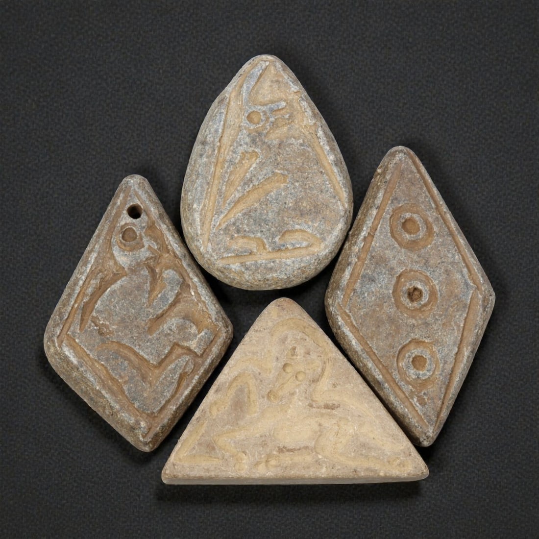Lot of 4 Ancient Near Eastern Schist Amulets, 82WP: A collection of four ancient Near Eastern amulets, carved from grey schist stone in varied geometric forms: diamond, teardrop, triangular, and lozenge shapes. Each piece is engraved with distinct moti