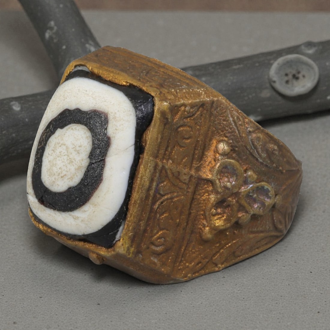 Antique Qajar Dynasty Gilt Evil Eye Ring, US Size 10, 15AJ: A gilt-metal ring of the Qajar period, US ring size 10, featuring a large square evil-eye glass inlay with a concentric black-and-white design (the glass exhibits age-related cracks). The bezel and wi