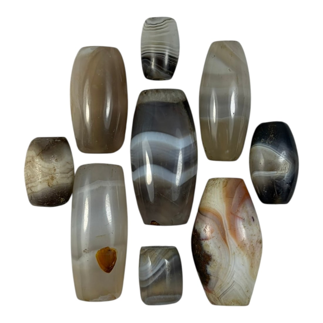A Lot of 9 Himalayan Banded Agate Beads, Ancient to Antique Period, 24YD: Comprising lot of barrel and ovoid beads, each carved from banded agate with natural tonal variations, many displaying characteristic concentric, linear, and dendritic patterns. The surfaces exhibit s