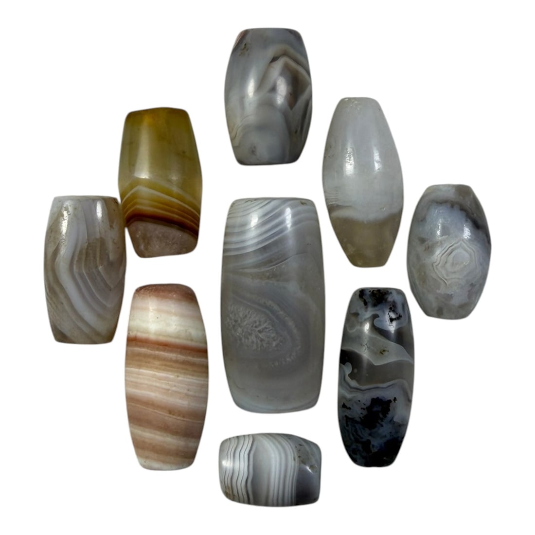 A Lot of 9 Himalayan Banded Agate Beads, Ancient to Antique Period, 33YD: Comprising lot of barrel and ovoid beads, each carved from banded agate with natural tonal variations, many displaying characteristic concentric, linear, and dendritic patterns. The surfaces exhibit s