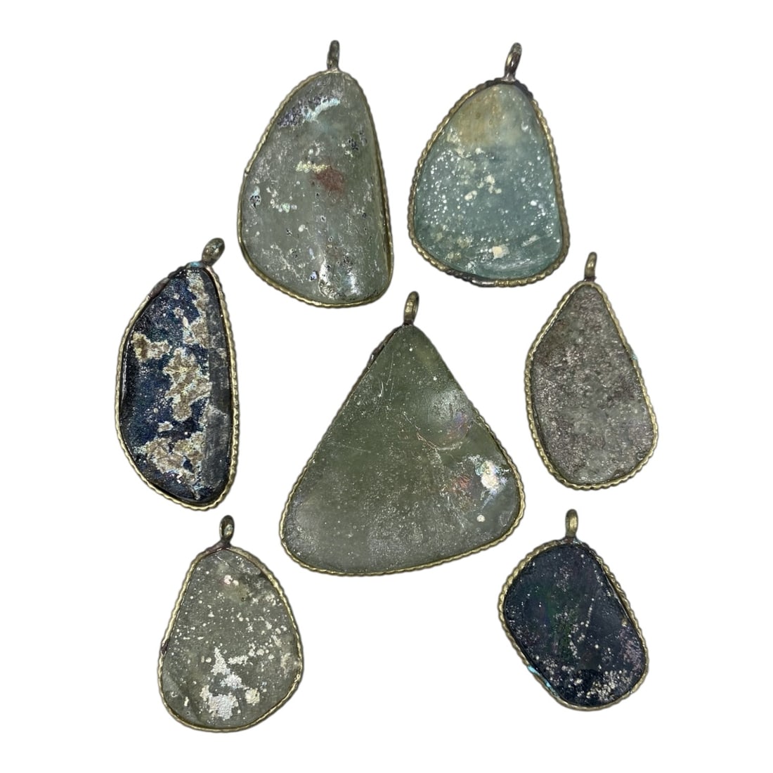 Lot of 7 Ancient Roman Glass Slag Pendants in Modern Brass Settings, 62AH: A collection of seven pendants featuring authentic ancient Roman glass slag fragments, set in modern brass settings. Each pendant showcases a unique, irregularly shaped piece of Roman glass, exhibitin