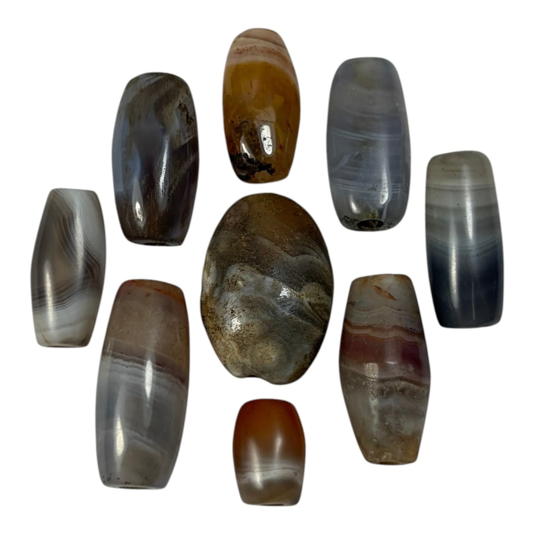 A Lot of 9 Himalayan Banded Agate Beads, Ancient to Antique Period, 53AN: Comprising lot of barrel and ovoid beads, each carved from banded agate with natural tonal variations, many displaying characteristic concentric, linear, and dendritic patterns. The surfaces exhibit s