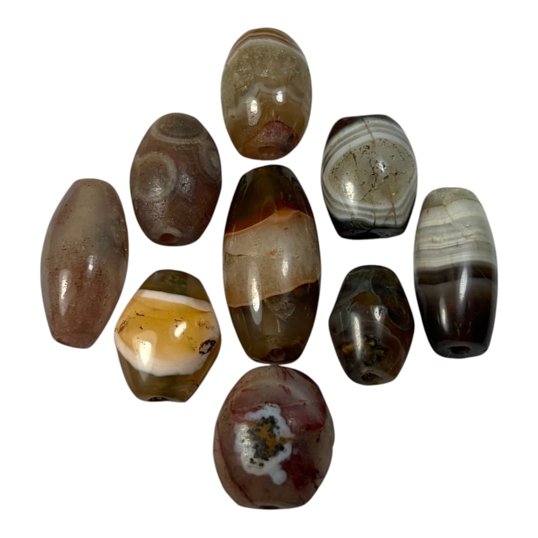 A Lot of 9 Himalayan Banded Agate Beads, Ancient to Antique Period, 46AN: Comprising lot of barrel and ovoid beads, each carved from banded agate with natural tonal variations, many displaying characteristic concentric, linear, and dendritic patterns. The surfaces exhibit s