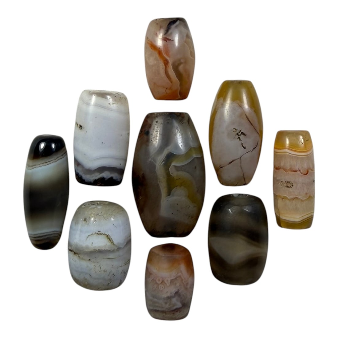 A Lot of 9 Himalayan Banded Agate Beads, Ancient to Antique Period, 30YD: Comprising lot of barrel and ovoid beads, each carved from banded agate with natural tonal variations, many displaying characteristic concentric, linear, and dendritic patterns. The surfaces exhibit s