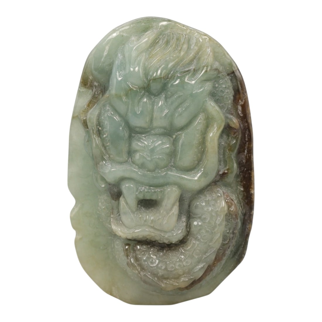 A Chinese Jadeite Jade Dragon Pendant, 20th Century, 8ZL: Carved from pale green jadeite with natural brownish inclusions along the edges, the object is formed as an irregularly oval pendant. The front is decorated in high relief with a dragon head, featurin
