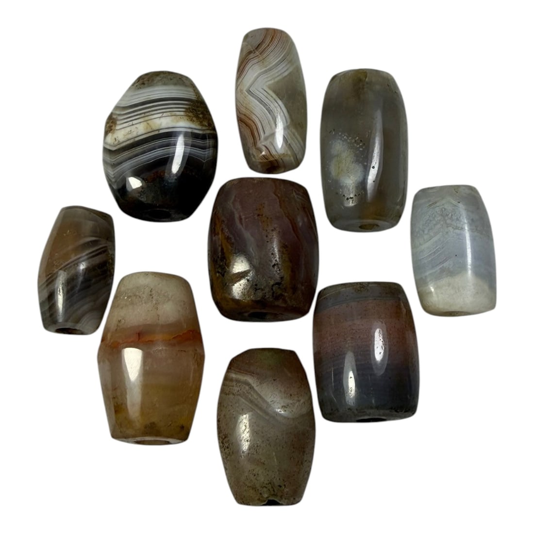 A Lot of 9 Himalayan Banded Agate Beads, Ancient to Antique Period, 51AN: Comprising lot of barrel and ovoid beads, each carved from banded agate with natural tonal variations, many displaying characteristic concentric, linear, and dendritic patterns. The surfaces exhibit s