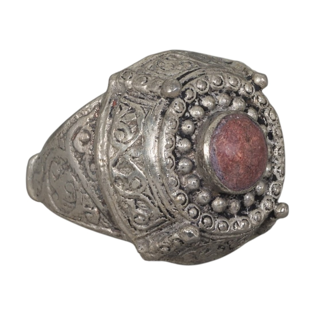 A Middle Eastern Silver Plated Red Jasper Ring, Late 19th-Early 20th Century, 22AK: The ring is centered with a round cabochon red jasper stone, set within a multi-layered domed bezel decorated with beaded granulation, wirework, and small raised finials at the corners. The bezel and 