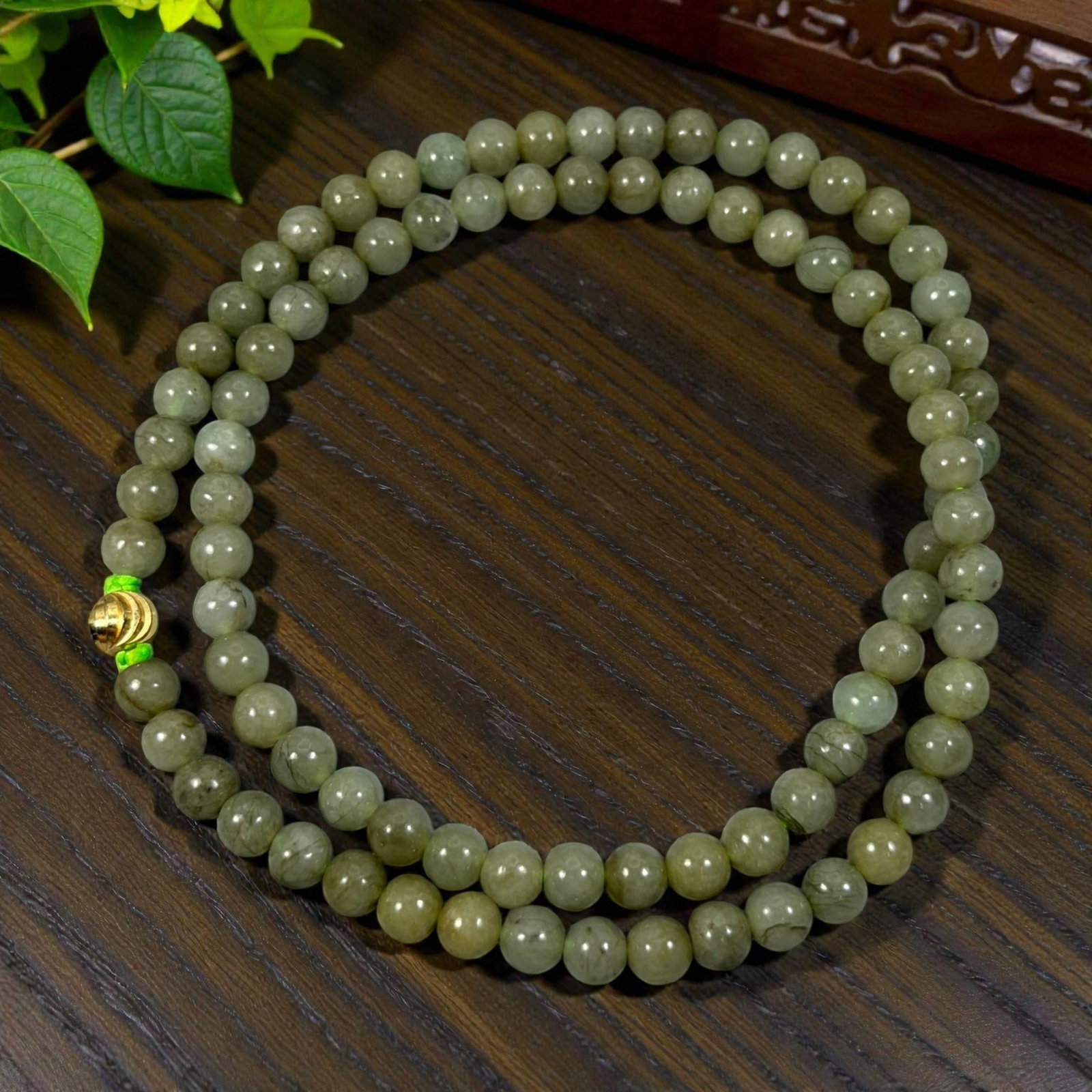 Chinese Jadeite Jade Bead Necklace, 20th Century, 100XE: A continuous strand of polished jadeite beads, each of uniform spherical form, displaying consistent muted olive-green tones with natural inclusions and subtle variations in translucency. The beads ar