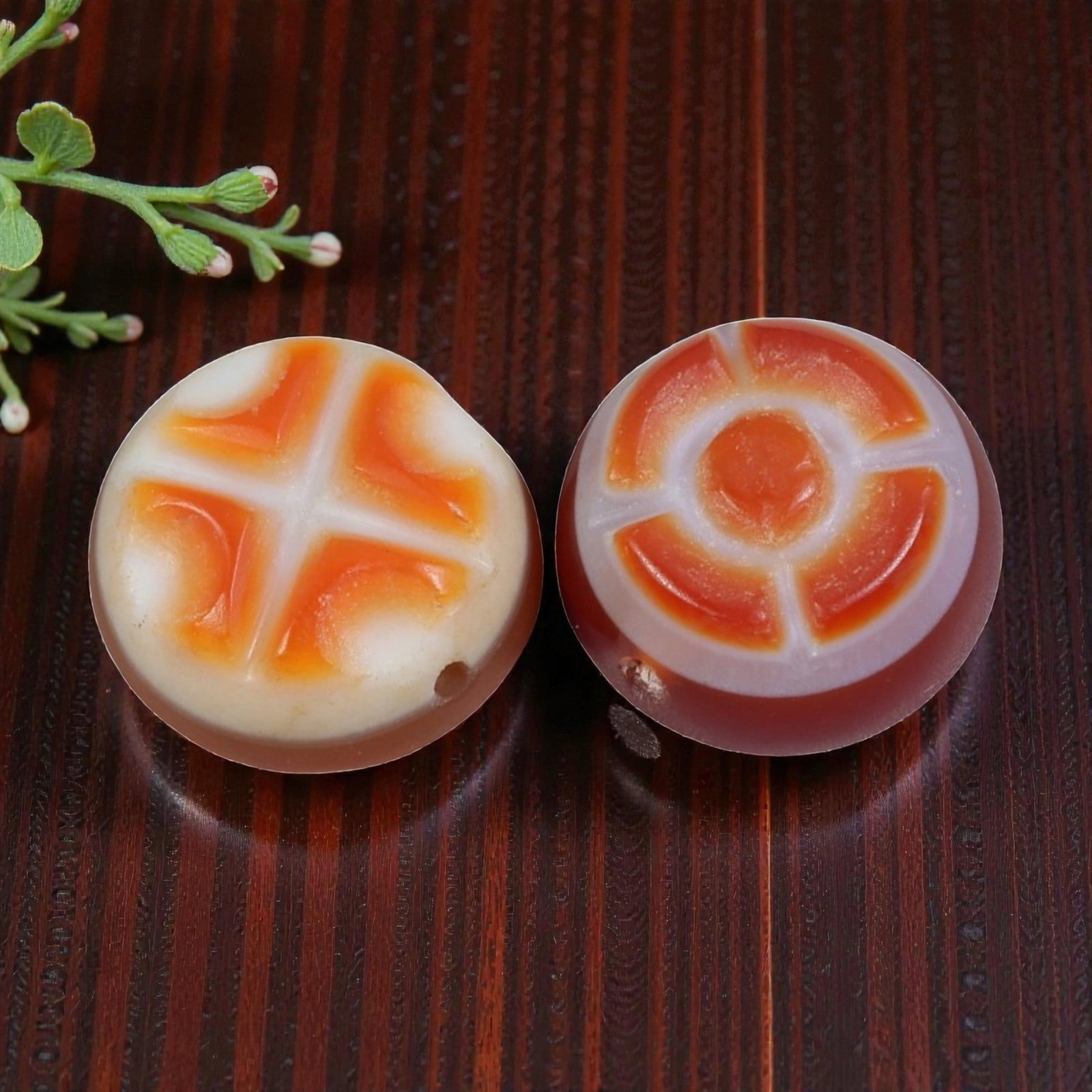 A Pair of Antique Himalayan Banded Carnelian Beads, 75AJ: The pair consists of two round, flat carnelian beads, each showcasing unique natural banding patterns. The left bead features a four-lobed cross motif in orange against a creamy white background, whil