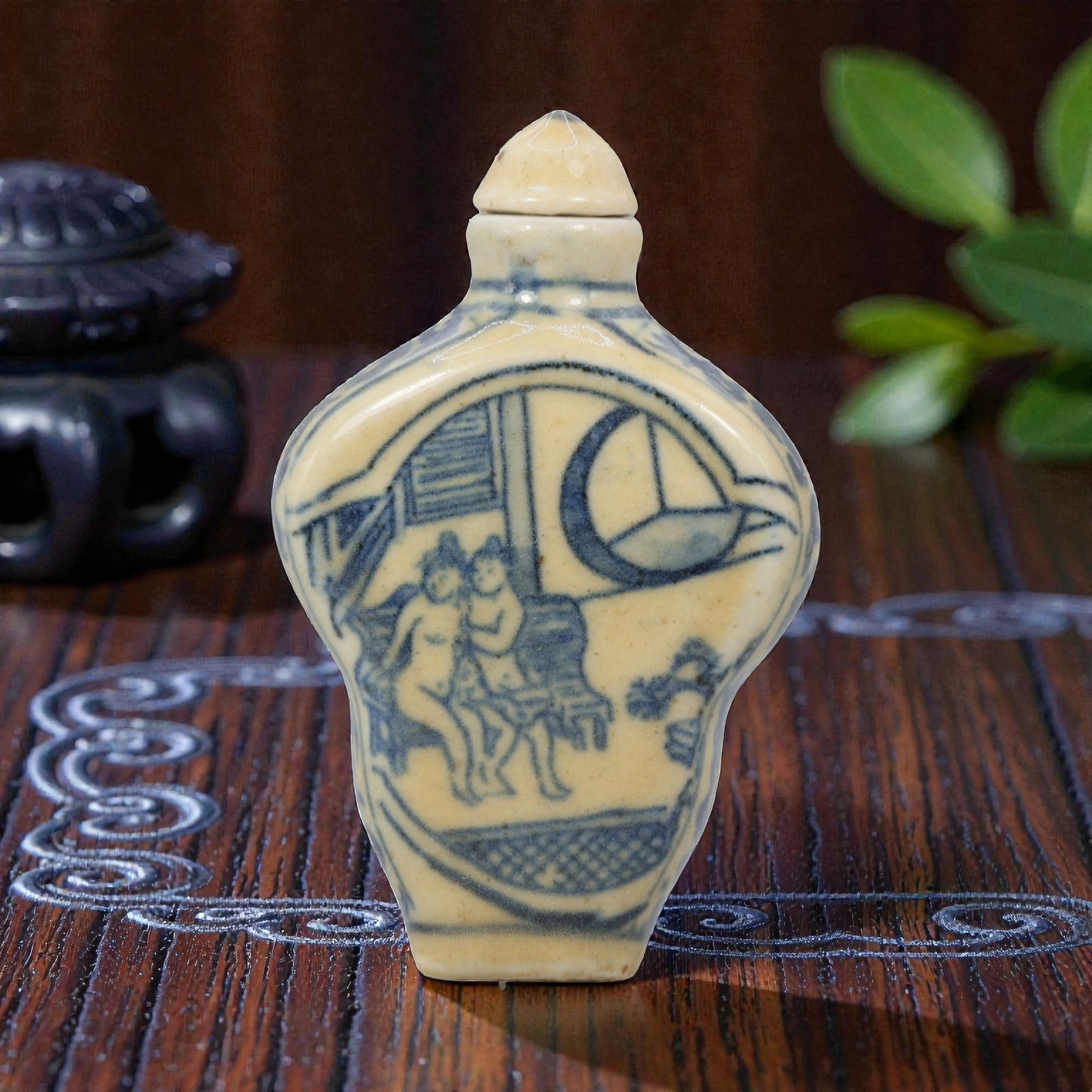A Chinese Porcelain Snuff Bottle, 20th Century, 12YD: Crafted from porcelain with a pale cream glaze and decorated in underglaze blue, the snuff bottle features a flattened, quatrefoil-shaped body, a short cylindrical neck, and a conical stopper. The mai