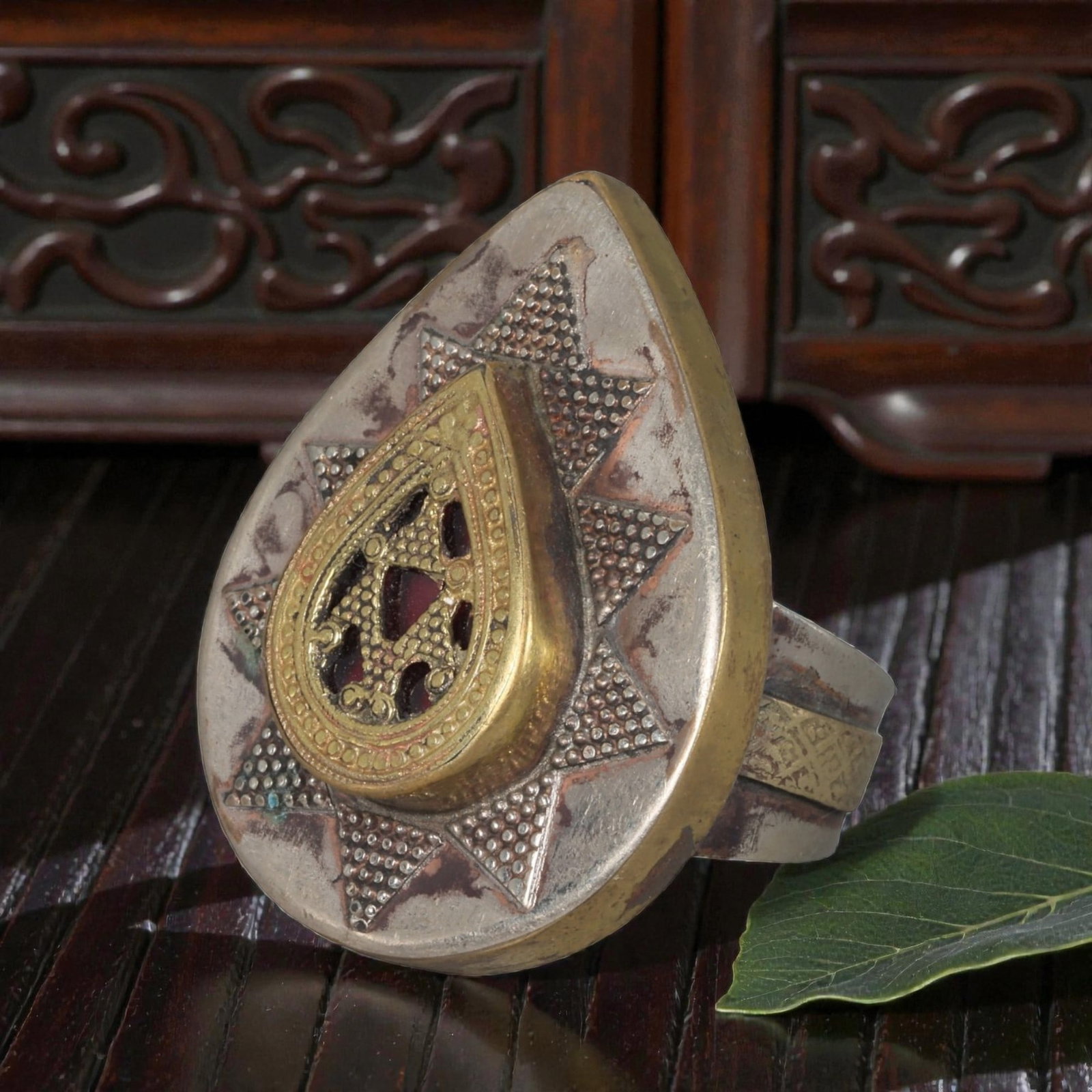 A Central Asian Silver Plated Teardrop Form Ring, Late 19th-Early 20th Century, 33AK: Crafted from silver plated metal with brass accents, featuring a wide, open band. The teardrop-shaped bezel displays a central raised teardrop panel with openwork detailing and a red inlay. The surrou
