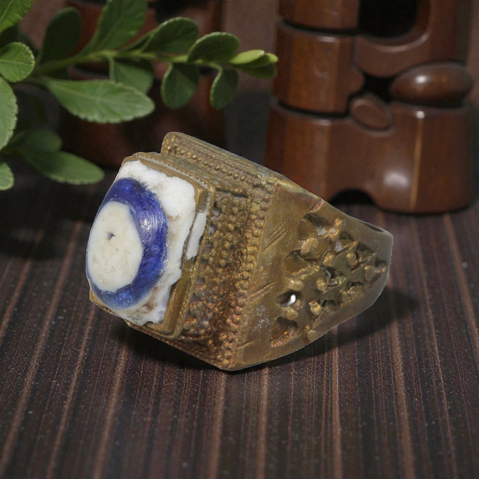 Antique Qajar Dynasty Gilt Evil Eye Ring, US Size 10, 14AJ: A gilt-metal ring of the Qajar period, US ring size 10, featuring a rectangular bezel set with a blue-and-white evil-eye glass inlay. The ring is richly detailed with multiple layers of ornamentation: