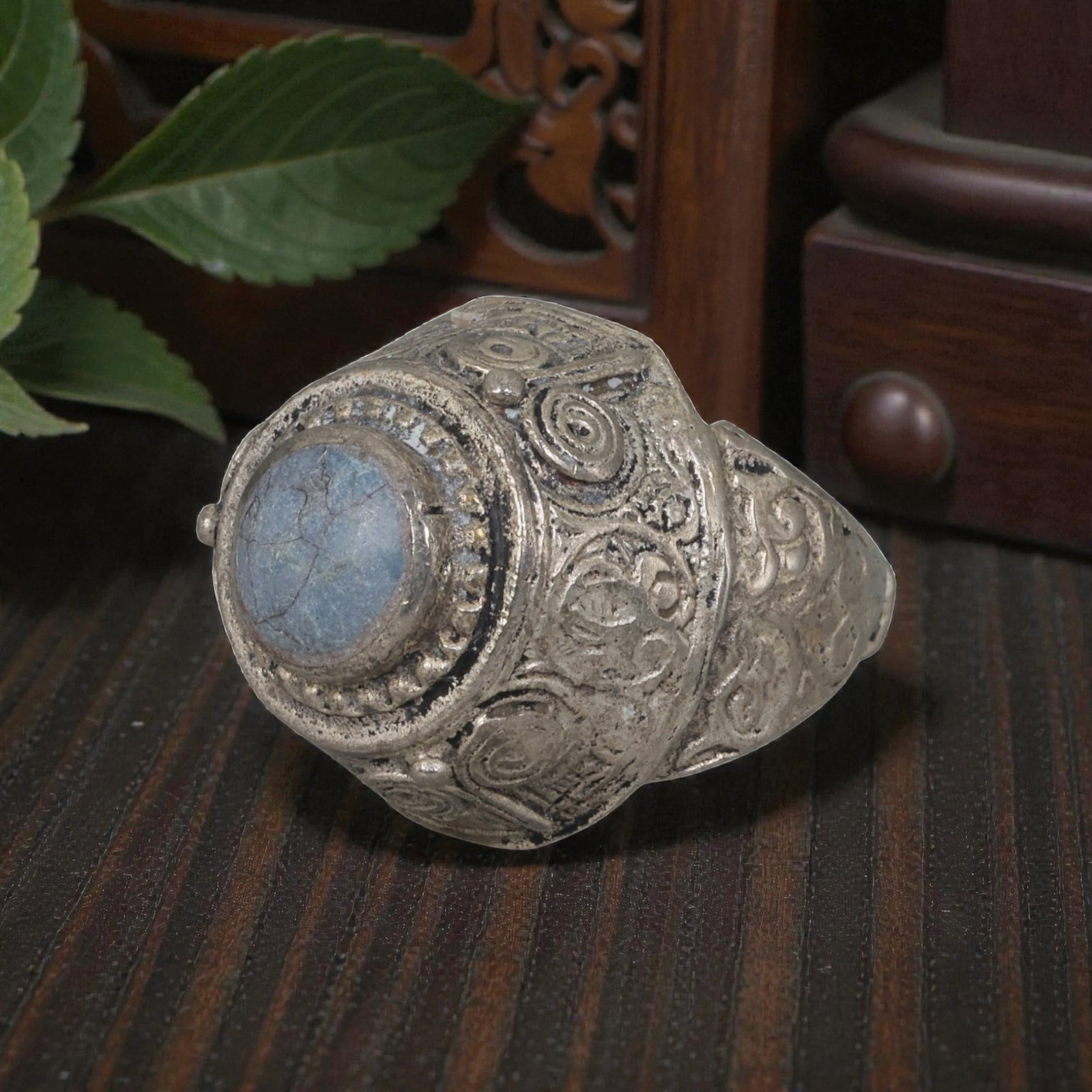 A Middle Eastern Silver Plated Turquoise Ring, Late 19th-Early 20th Century, 15AK: The ring is centered with a round cabochon turquoise stone exhibiting natural light blue tones and surface veining, set within a domed bezel framed by a beaded border. The bezel and shoulders are engr