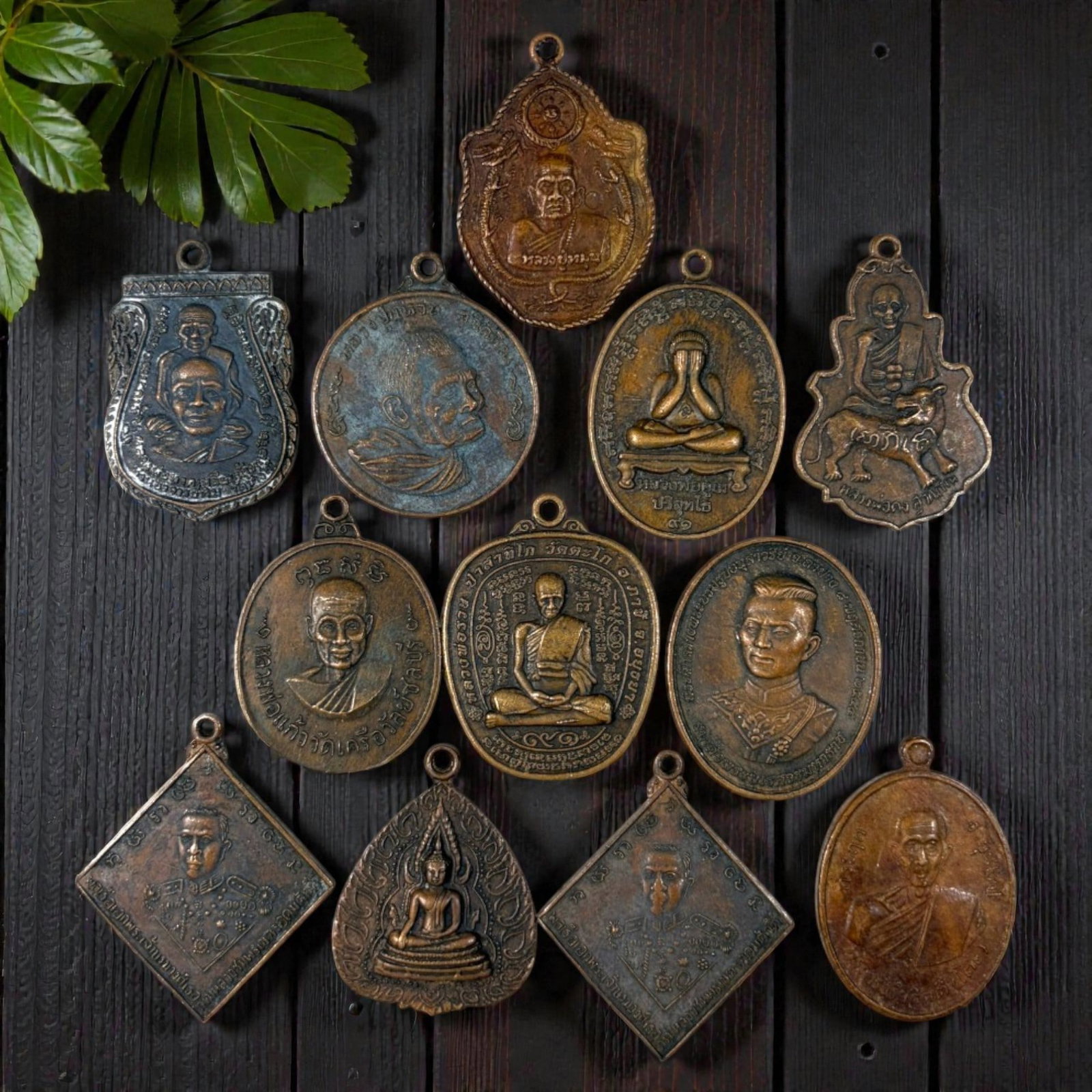 A Lot of 12 Vintage Thai Copper and Bronze Amulets, 48AA: Comprising 12 unmounted pendants ranging from 3.5 to 4 cm in height. The collection features a diverse array of cast metal amulets, including monastic portraits, revered royal figures, and sacred Budd