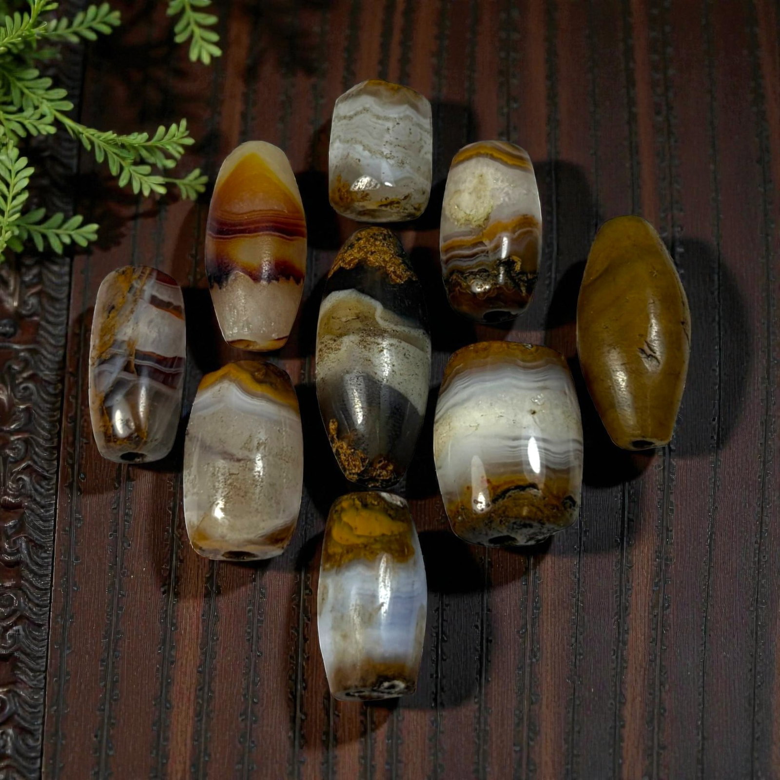 A Lot of 9 Himalayan Banded Agate Beads, Ancient to Antique Period, 45AN: Comprising lot of barrel and ovoid beads, each carved from banded agate with natural tonal variations, many displaying characteristic concentric, linear, and dendritic patterns. The surfaces exhibit s