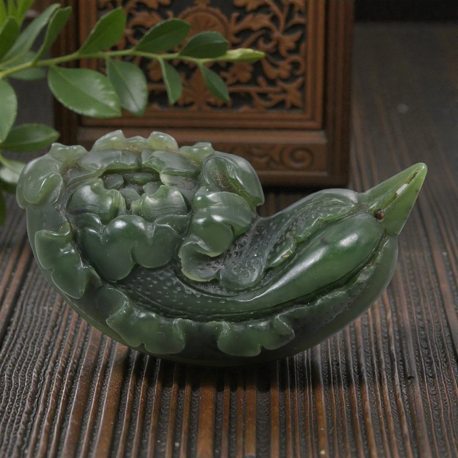 A Chinese Nephrite Jade Flower-Form Ornament, 20th Century, 31FA: Carved from dark green nephrite jade with lighter translucent areas and natural inclusions, the object is worked in the form of a flowering plant shown in low relief. The composition is horizontally o