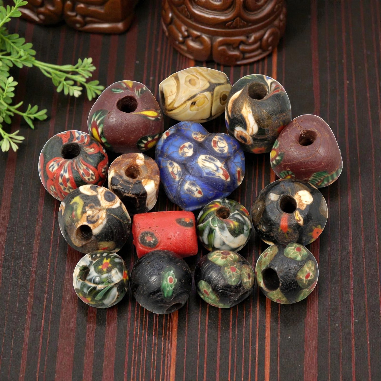 A Lot of 15 Antique/ Vintage Artisan Glass Trade Beads, 28WM: A curated collection of 15 glass trade beads, varying in form from spherical, barrel, and heart-shaped to polygonal, all with central perforations. The beads feature intricate mosaic, trailed, and app