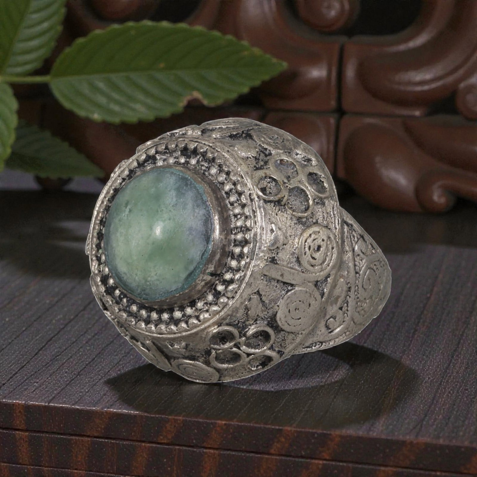 A Middle Eastern Silver Plated Green Agate Ring, Late 19th-Early 20th Century, 23AK: The ring is centered with a round cabochon green agate stone exhibiting natural mottled green tones, set within a domed bezel framed by beaded granulation. The bezel and shoulders are decorated with a