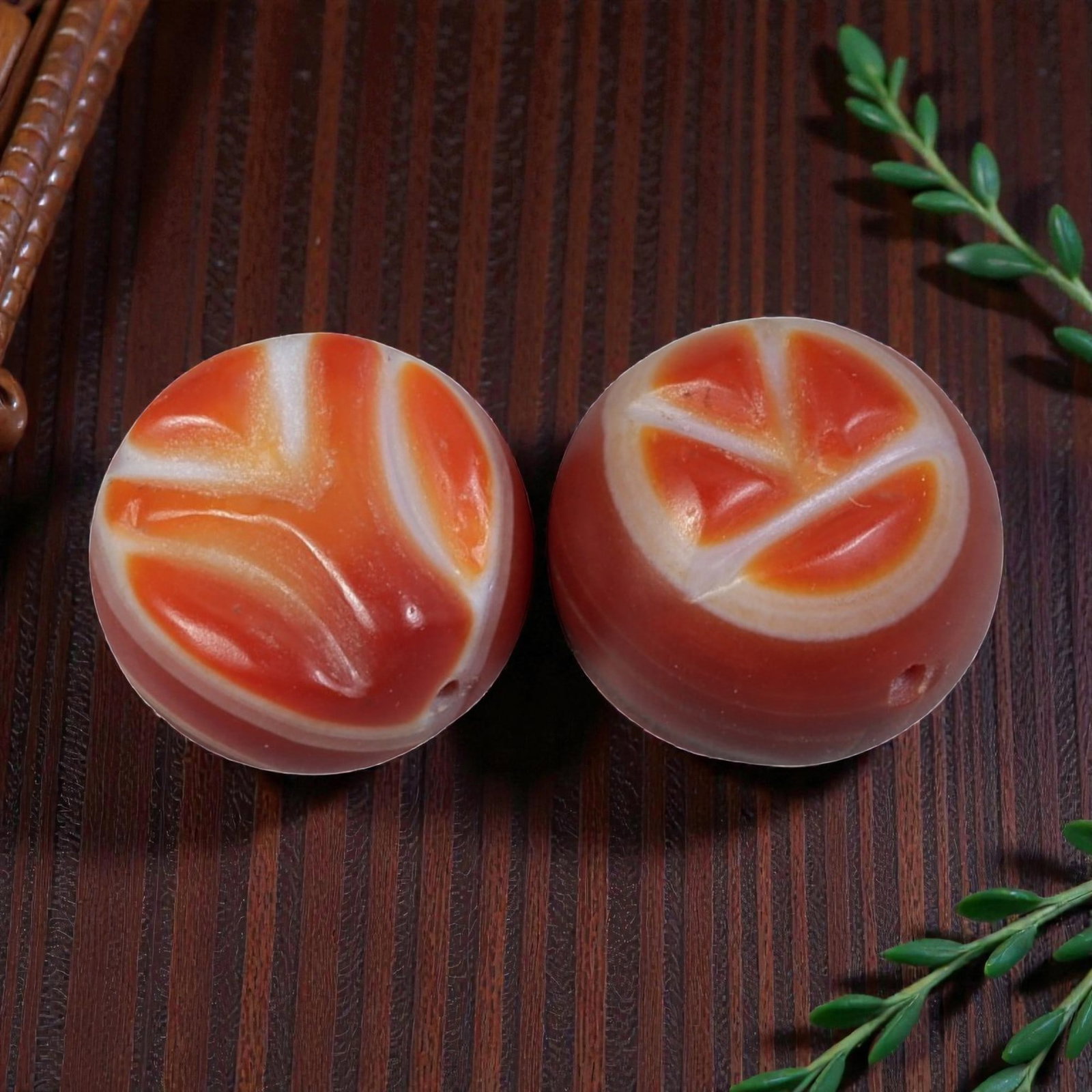 A Pair of Antique Himalayan Banded Carnelian Beads, 76AJ: The pair consists of two round carnelian beads, each displaying unique natural banding patterns. The left bead features flowing, abstract orange and white striations, while the right bead shows a fan-