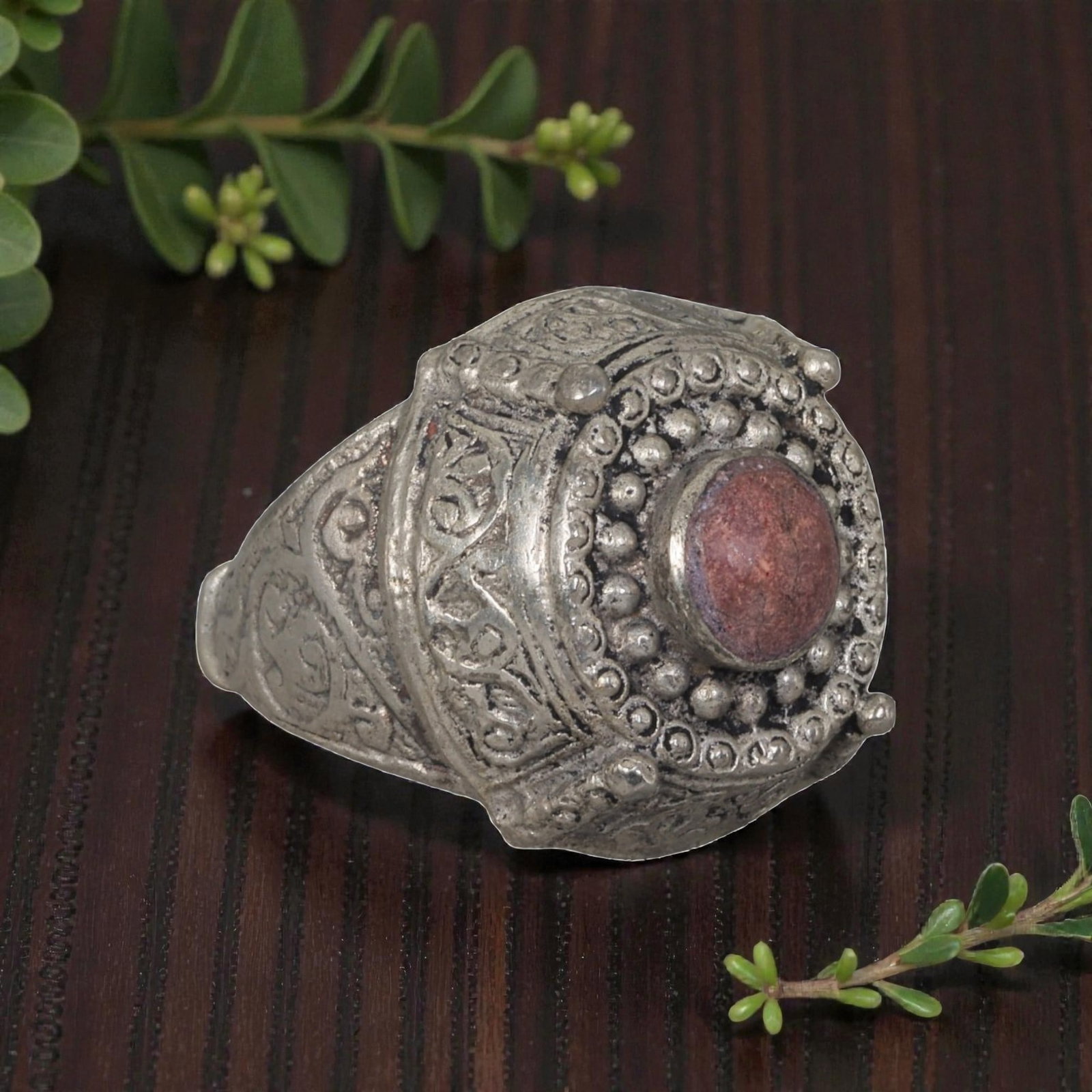 A Middle Eastern Silver Plated Red Jasper Ring, Late 19th-Early 20th Century, 22AK: The ring is centered with a round cabochon red jasper stone, set within a multi-layered domed bezel decorated with beaded granulation, wirework, and small raised finials at the corners. The bezel and 