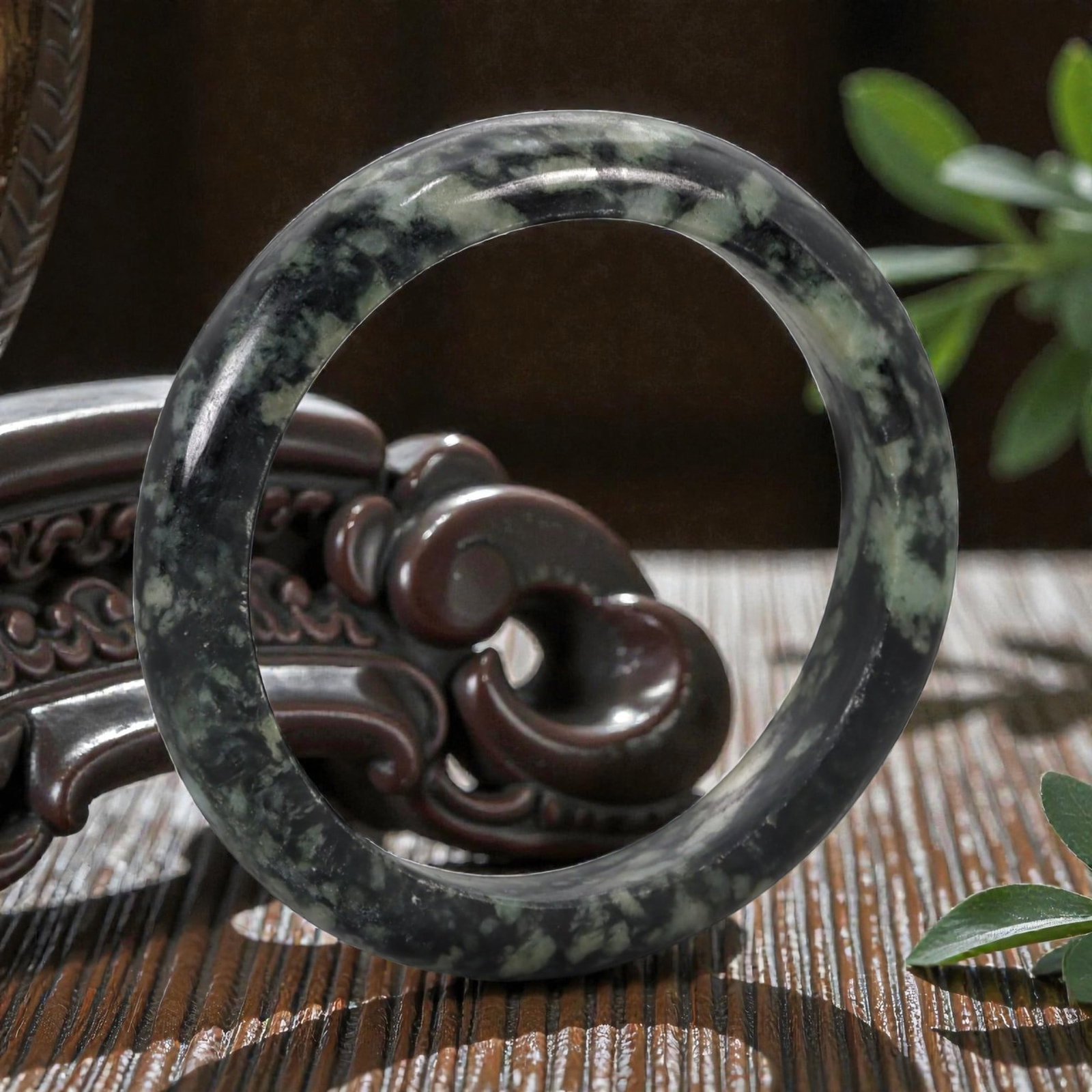 A Chinese Jadeite Jade Bangle Bracelet, 20th Century, 95ZK: Carved from jadeite jade with a deep blackish-green base and irregular pale green and creamy-white mottling throughout, the bangle is formed as a solid circular band with a flattened rounded cross-sec