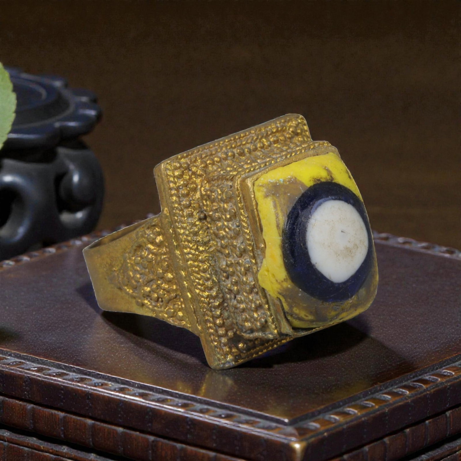 Antique Qajar Dynasty Gilt Evil Eye Ring, US Size 8, 53AJ: A gilt-metal ring of the Qajar period, US ring size 8, featuring a large square evil-eye glass inlay with a vibrant yellow, blue, and white concentric design. The bezel and band are adorned with intri