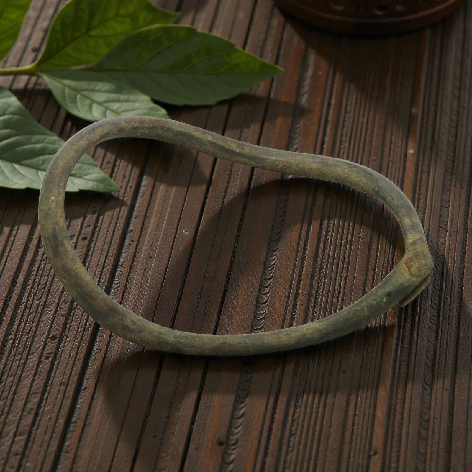 Ancient Bronze Anklet - Roman Penannular Bangle, 82BN: A penannular bronze anklet of ancient Roman origin, formed from a slender, rounded bronze band. The piece features a simple folded terminal closure at one end, characteristic of Roman provincial jewel