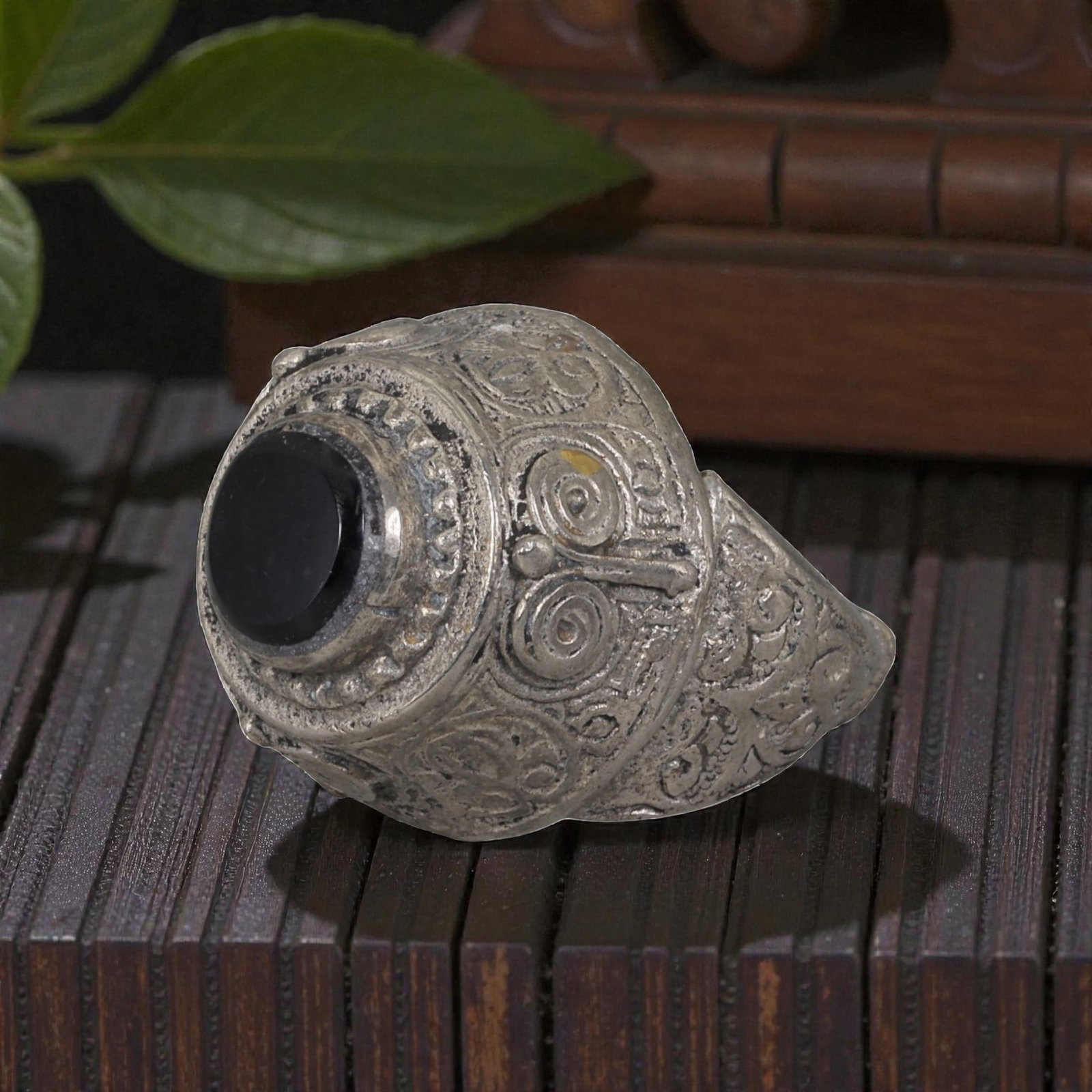 A Middle Eastern Silver Plated Onyx Ring, Late 19th-Early 20th Century, 25AK: The ring is centered with a round cabochon onyx stone set within a domed bezel framed by a raised beaded border. The bezel and shoulders are engraved with stylized spiral and foliate motifs. The silve