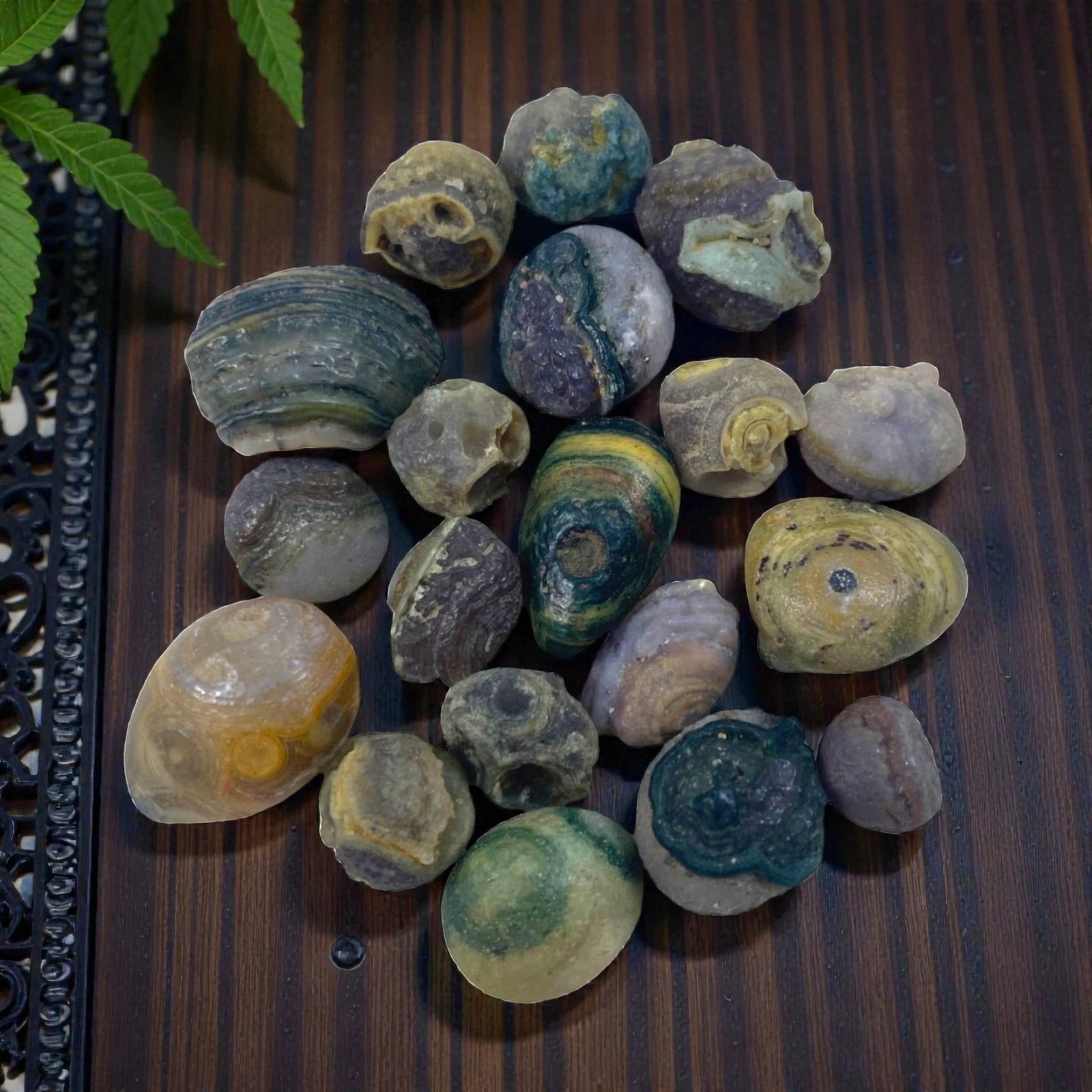 Lot of 19 Sino-Mongolian Agate Eye Beads, 97AC: Each bead is formed from naturally weathered agate, displaying varied earthy tones including greens, blues, purples, yellows, and grays. Many examples feature characteristic concentric banding and "ey