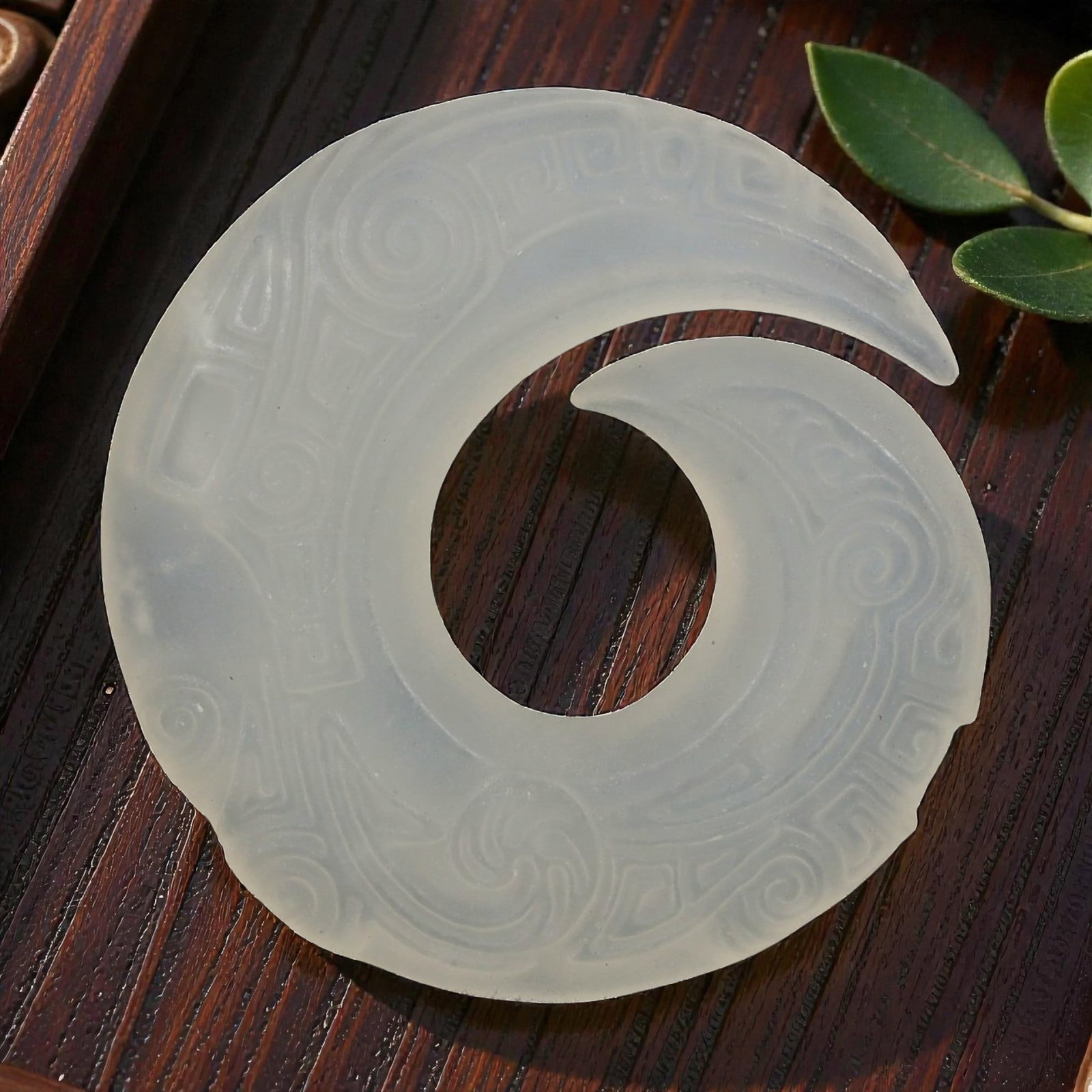 A Chinese Pale Jade Openwork Pendant, 20th Century, 92FD: Carved from translucent pale jade of even milky tone, the pendant is worked as a circular openwork form with an inward curling projection, creating a continuous flowing silhouette. The surface is deco
