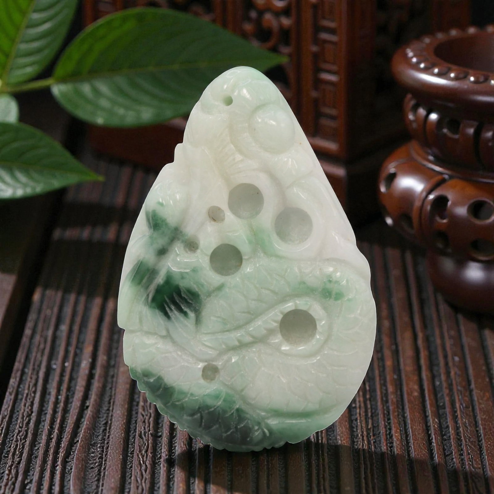 A Chinese Jadeite Jade Dragon Pendant, 20th Century, 9ZL: Carved from white jadeite with prominent green inclusions, the object is formed as a teardrop-shaped pendant. The front is decorated in openwork relief with a coiled dragon, featuring incised scale pa