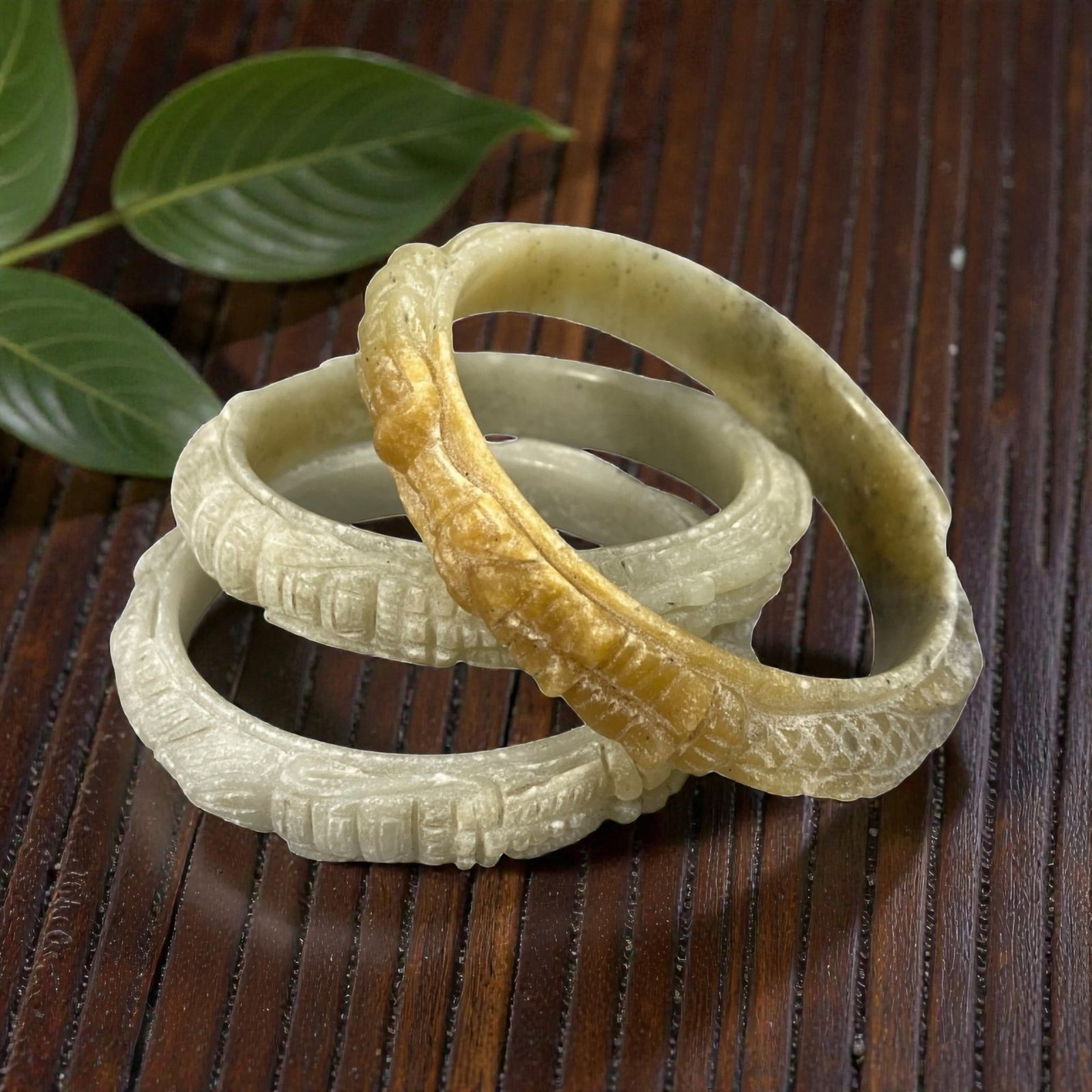 Lot of 3 Chinese Carved Jadeite Jade Dragon Bracelets (Bangles), 88AC: Each bracelet is carved from jadeite, displaying natural color variations including pale grey-green and warm yellowish-brown with mottling and inclusions. The outer surfaces are adorned with raised re