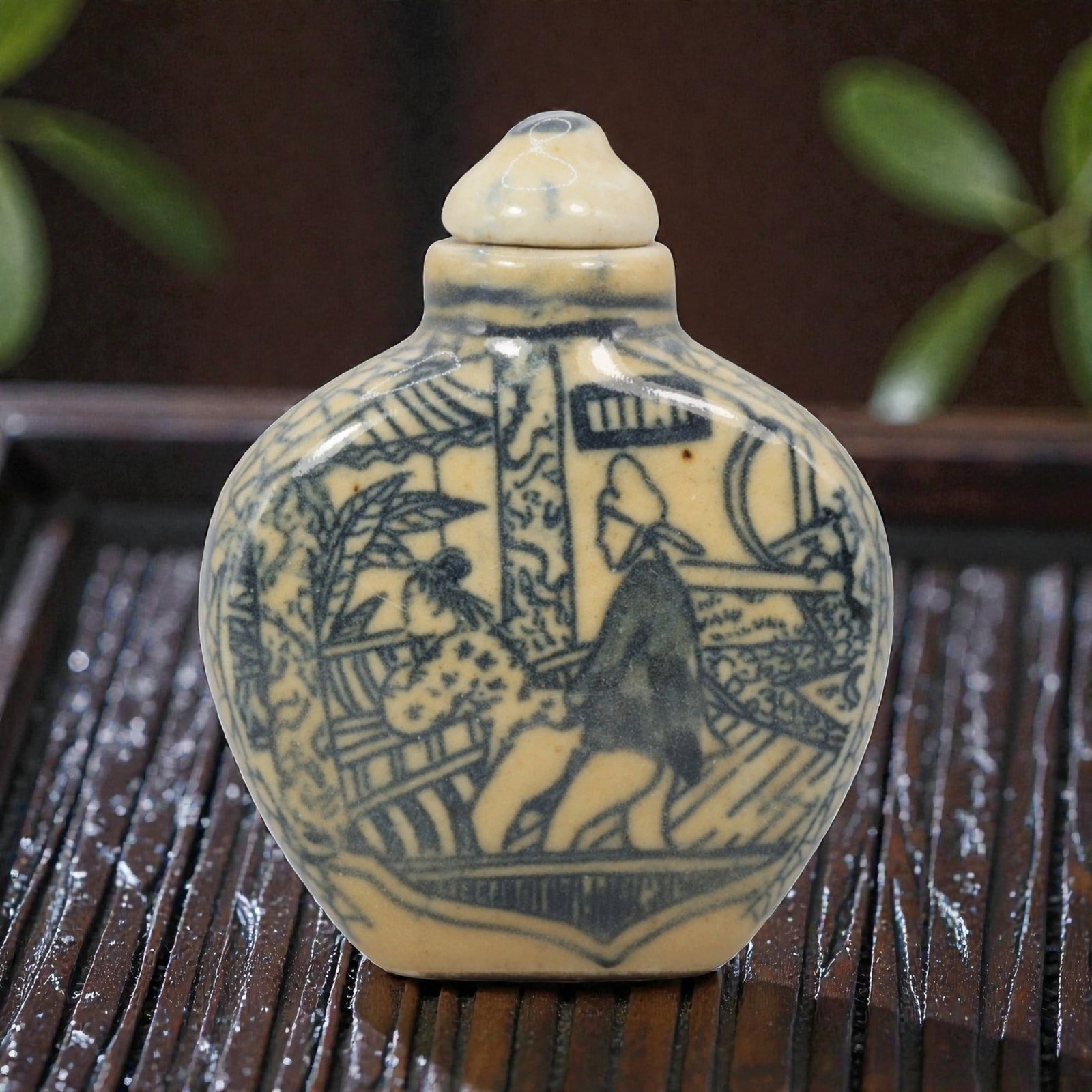 A Chinese Porcelain Snuff Bottle, 20th Century, 2YD: Made of porcelain with a pale yellowish glaze and underglaze blue decoration, the snuff bottle has a flattened, rounded body, a short cylindrical neck, and a matching domed stopper. The main surface i