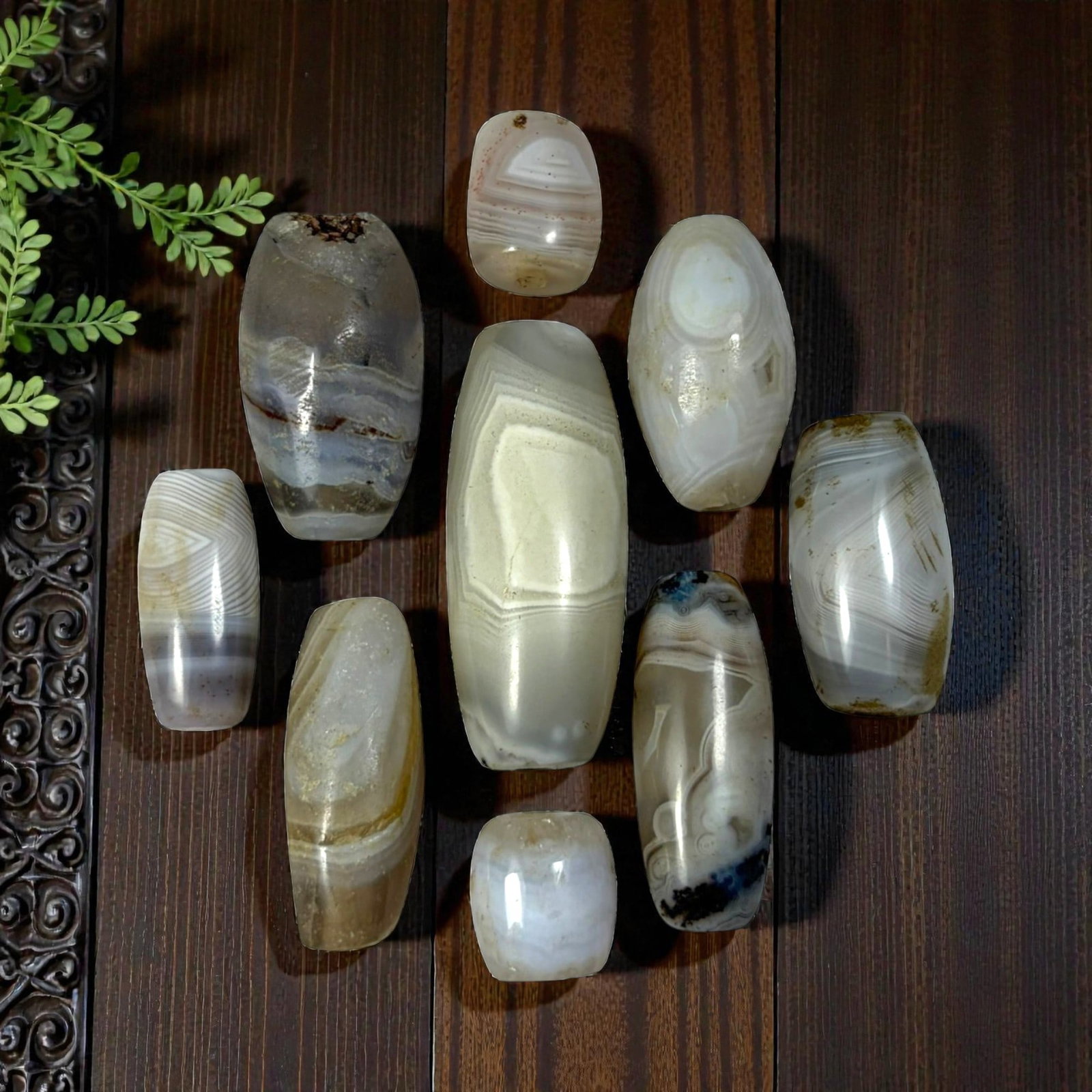 A Lot of 9 Himalayan Banded Agate Beads, Ancient to Antique Period, 38AN: Comprising lot of barrel and ovoid beads, each carved from banded agate with natural tonal variations, many displaying characteristic concentric, linear, and dendritic patterns. The surfaces exhibit s