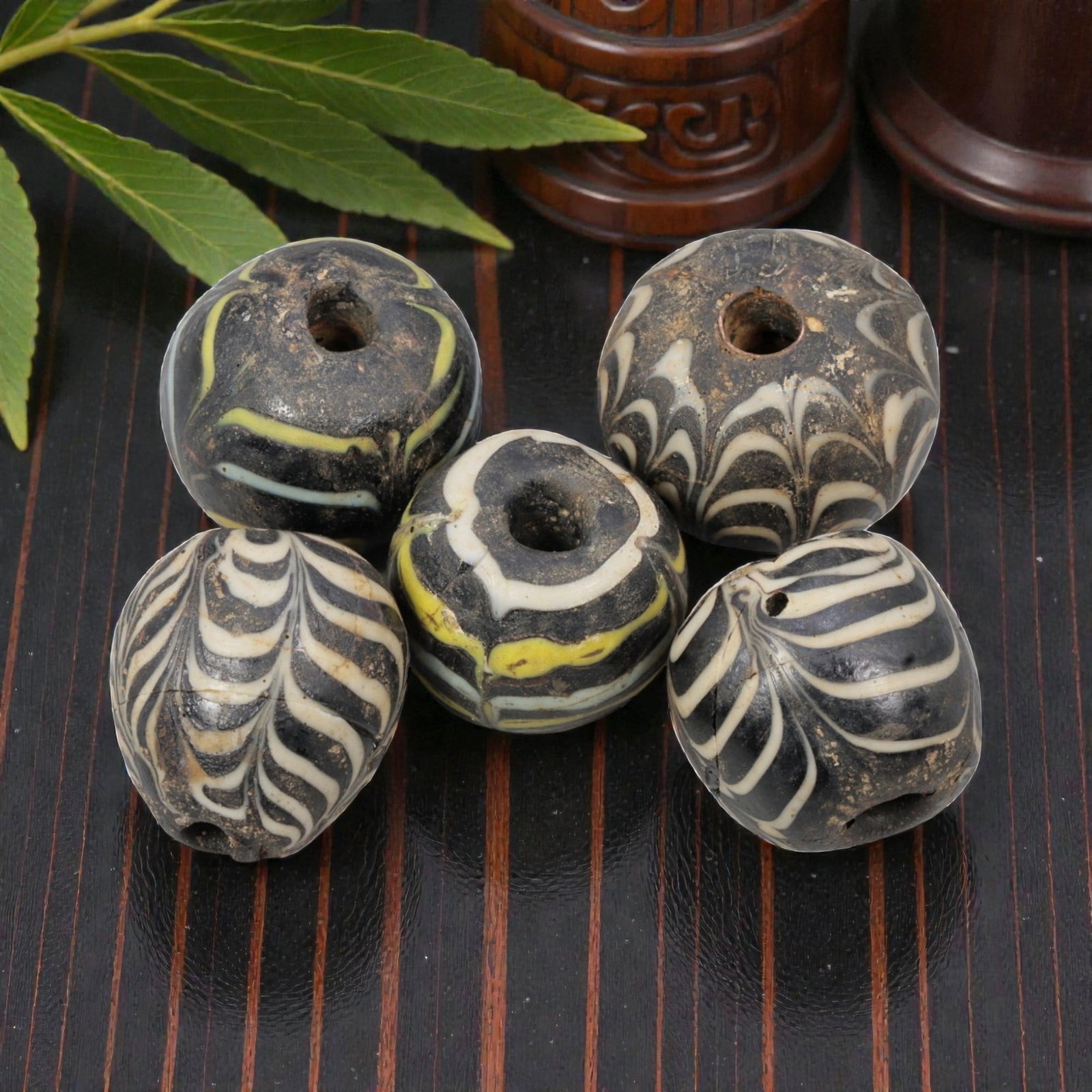 Lot of 5 Antique Islamic Feather-Patterned Glass Beads, Circa 9th-14th Century, 75AD: Comprising five beads of varying sizes, ranging from 1.5 cm (5/8 in.) to 2 cm (3/4 in.), each formed from dark base glass with applied feather-patterned decoration. Three beads feature black glass wit