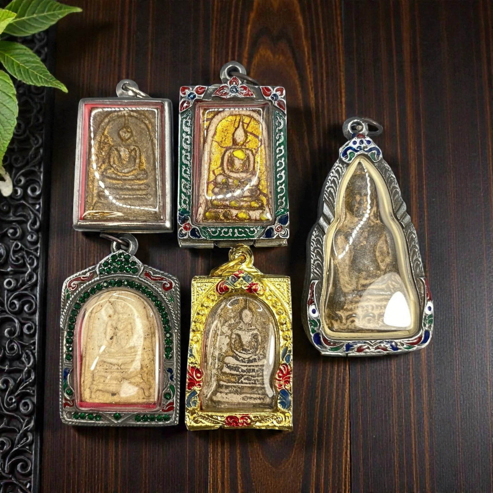 A Lot of 5 Vintage Thai Buddhist Amulets with Enamel and Jewel Accents, 14WT: A curated lot of five vintage Thai Buddhist amulets, each encased in decorative metal frames with enamel detailing and jewel accents. The amulets depict traditional seated Buddha iconography, with var