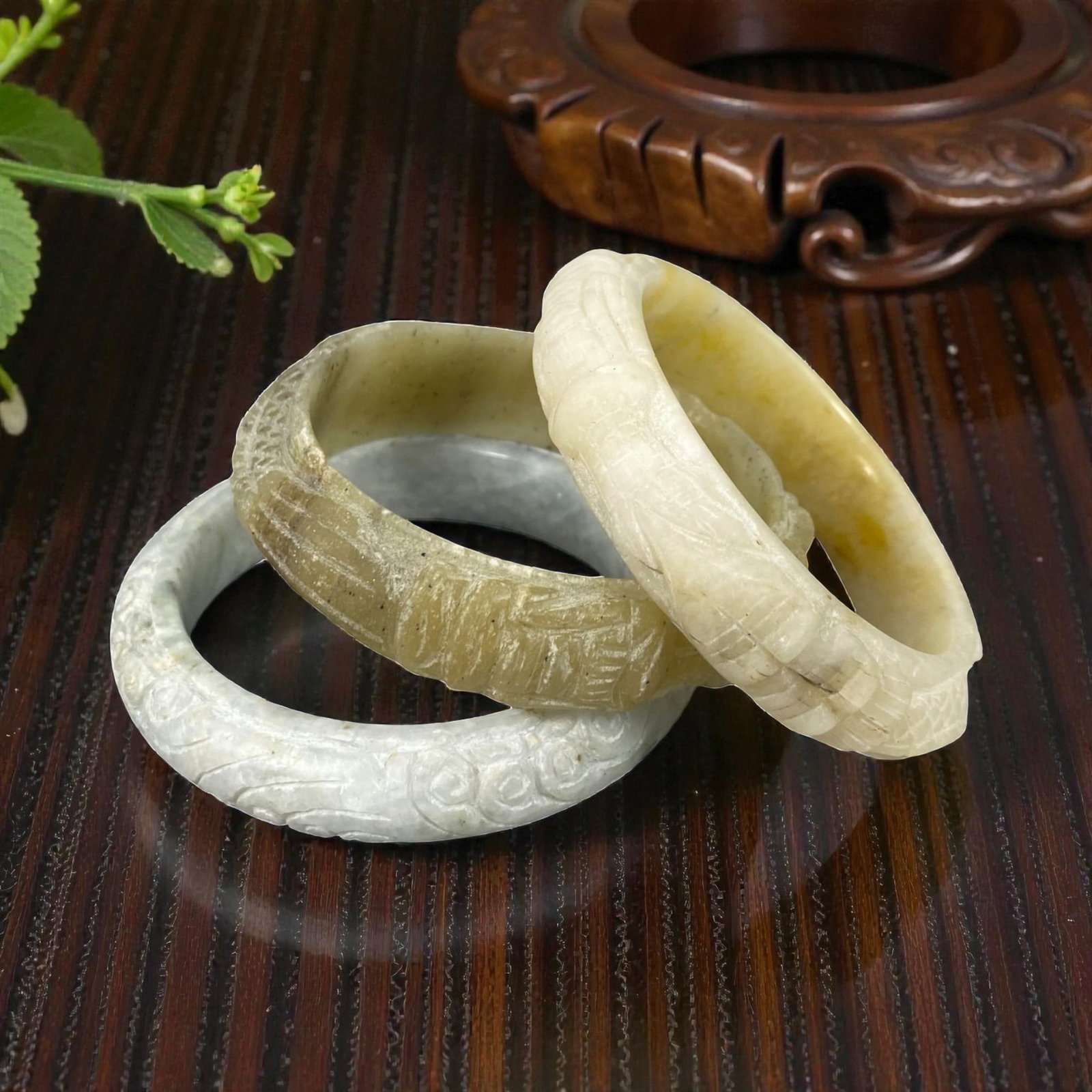 Lot of 3 Chinese Carved Jadeite Jade Bracelets (Bangles), 90AC: Each bracelet is carved from jadeite with varied natural coloration and inclusions, including pale grey-white, mottled greyish-brown, and creamy white with yellowish tones. The outer surfaces feature 