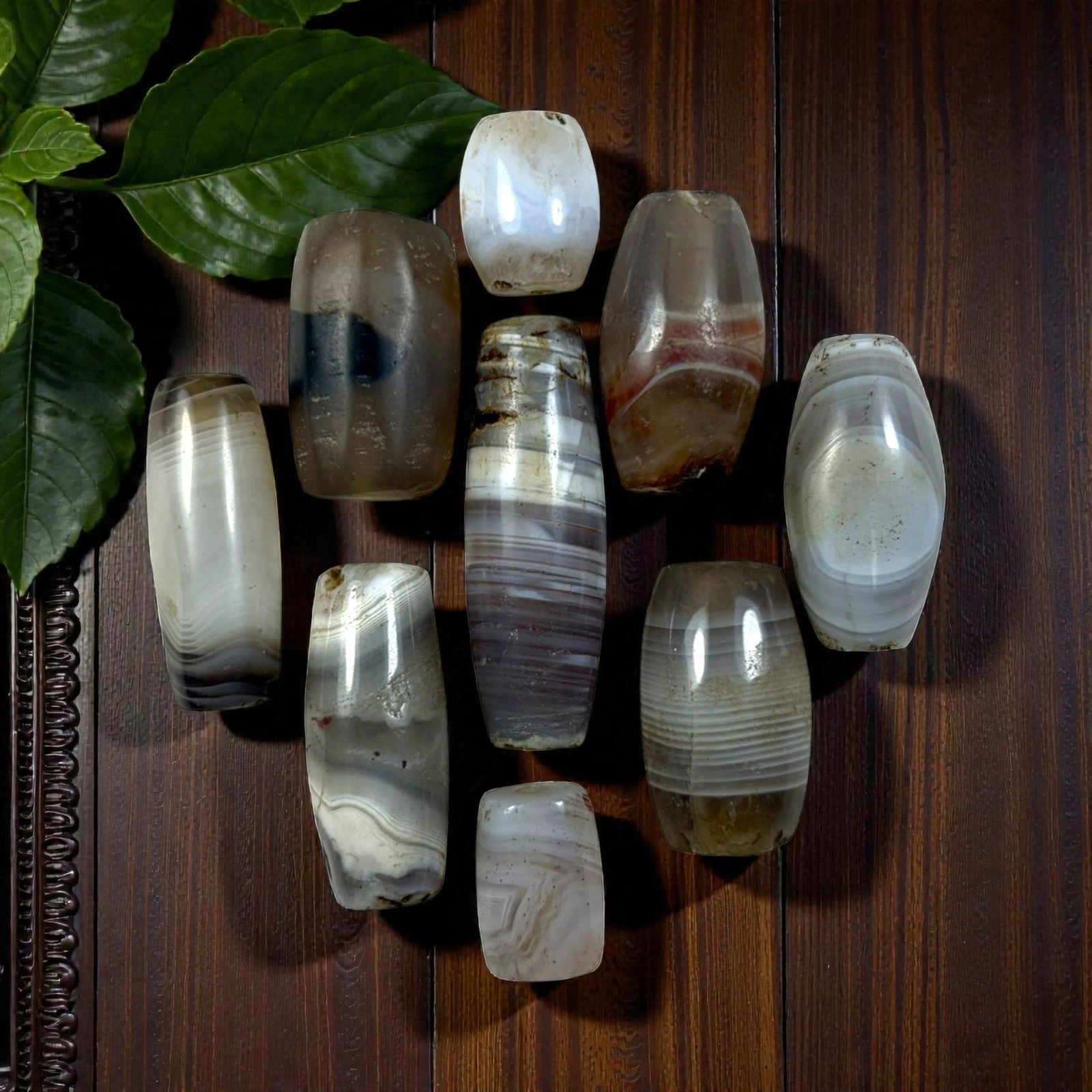A Lot of 9 Himalayan Banded Agate Beads, Ancient to Antique Period, 32YD: Comprising lot of barrel and ovoid beads, each carved from banded agate with natural tonal variations, many displaying characteristic concentric, linear, and dendritic patterns. The surfaces exhibit s