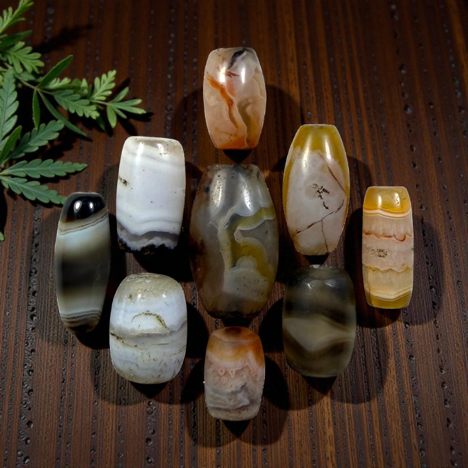 A Lot of 9 Himalayan Banded Agate Beads, Ancient to Antique Period, 30YD: Comprising lot of barrel and ovoid beads, each carved from banded agate with natural tonal variations, many displaying characteristic concentric, linear, and dendritic patterns. The surfaces exhibit s