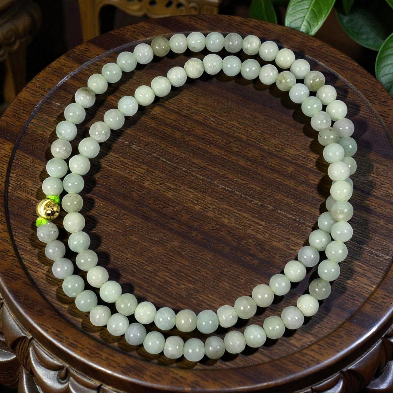 Chinese Jadeite Jade Bead Necklace, 20th Century, 99XE: A continuous strand of polished jadeite beads, each of uniform spherical form, displaying soft pale green, off-white, and light grey tones with natural inclusions and subtle variations in translucency